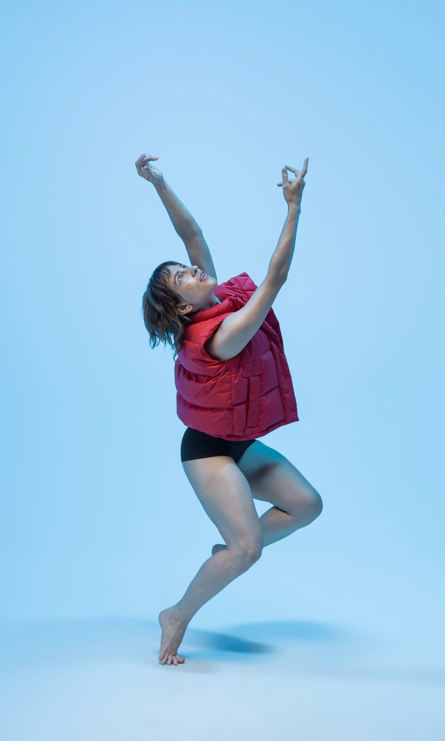 A circular studio portrait of dancer Non Edwards reaching upward gracefully mid-movement against a clear blue backdrop.