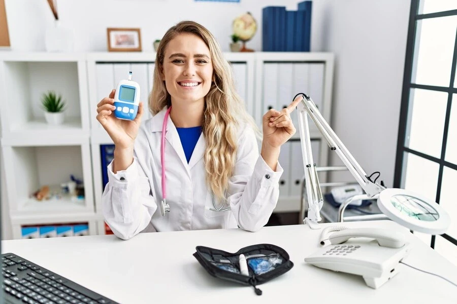 doctor woman holding glucose meter smiling happy pointing with hand and finger to the side