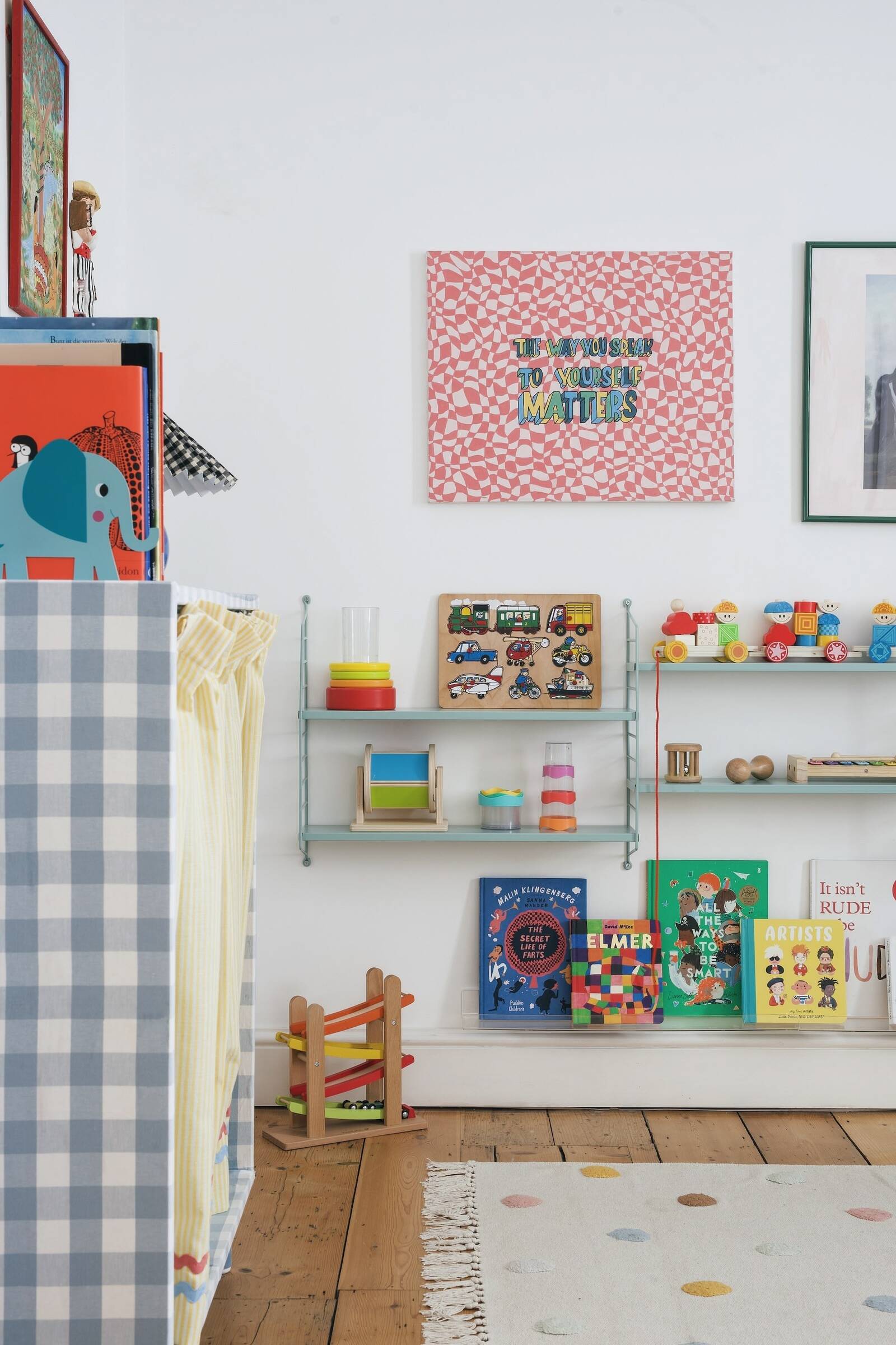 A children's playroom with books, toys, and artwork on white walls, including a pink patterned sign, showing that children's spaces can be both elevated and fun!