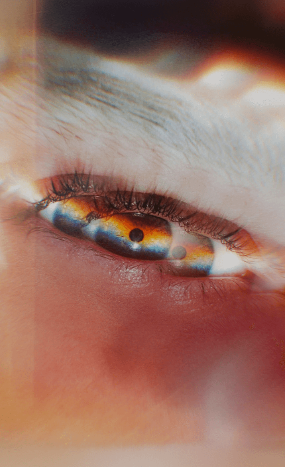  An extreme close-up of a human eye with a dreamlike, prismatic light effect creating rainbow colors across the iris and lens flare around the edges