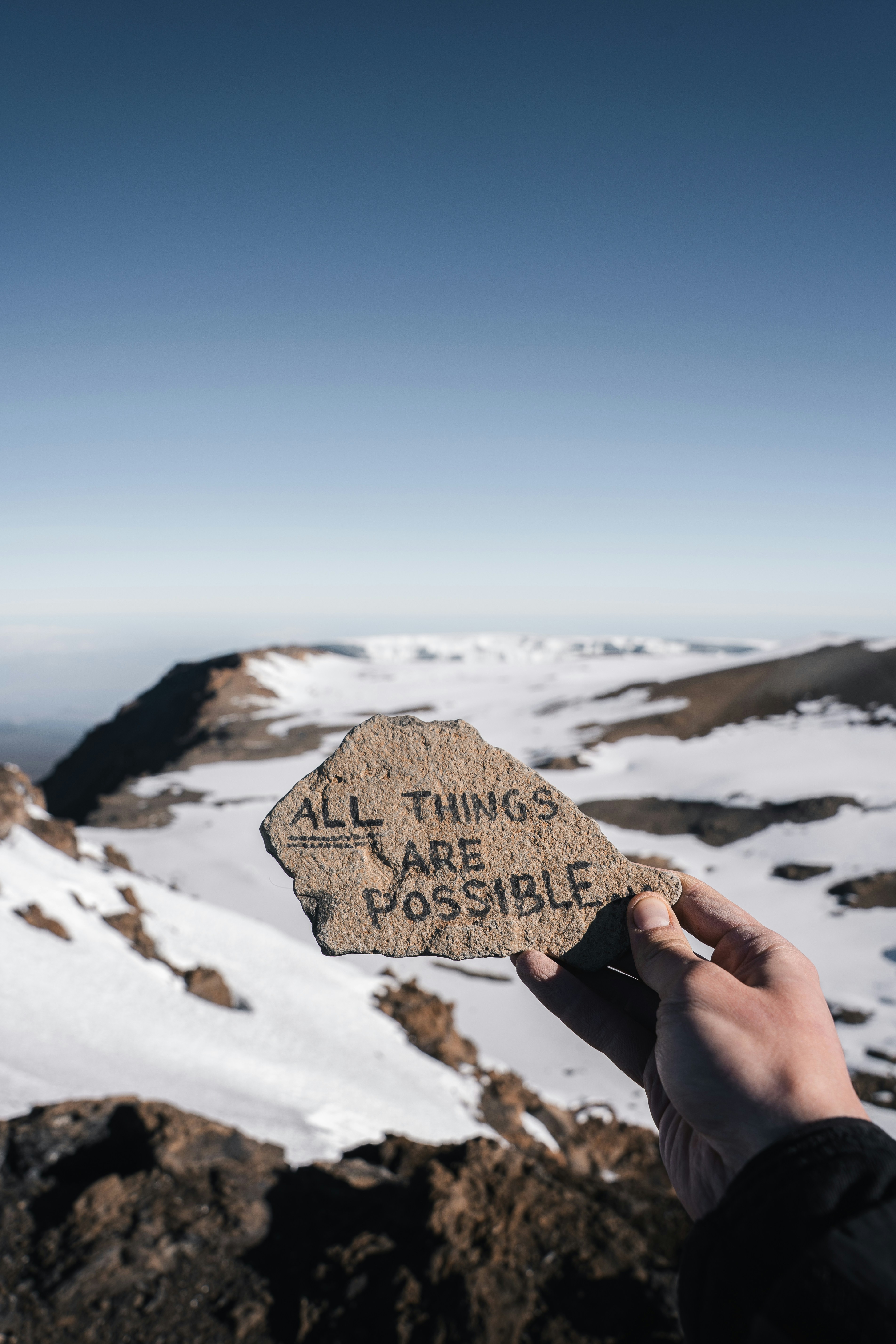 Person holds rock with encouraging message on snowy mountain.