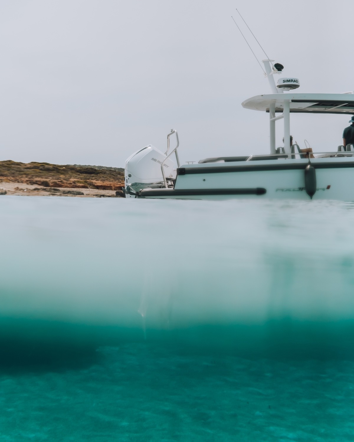 White Axopar 37 motor yacht anchored in crystal-clear turquoise waters beside dramatic limestone cliffs in the Cyclades.
