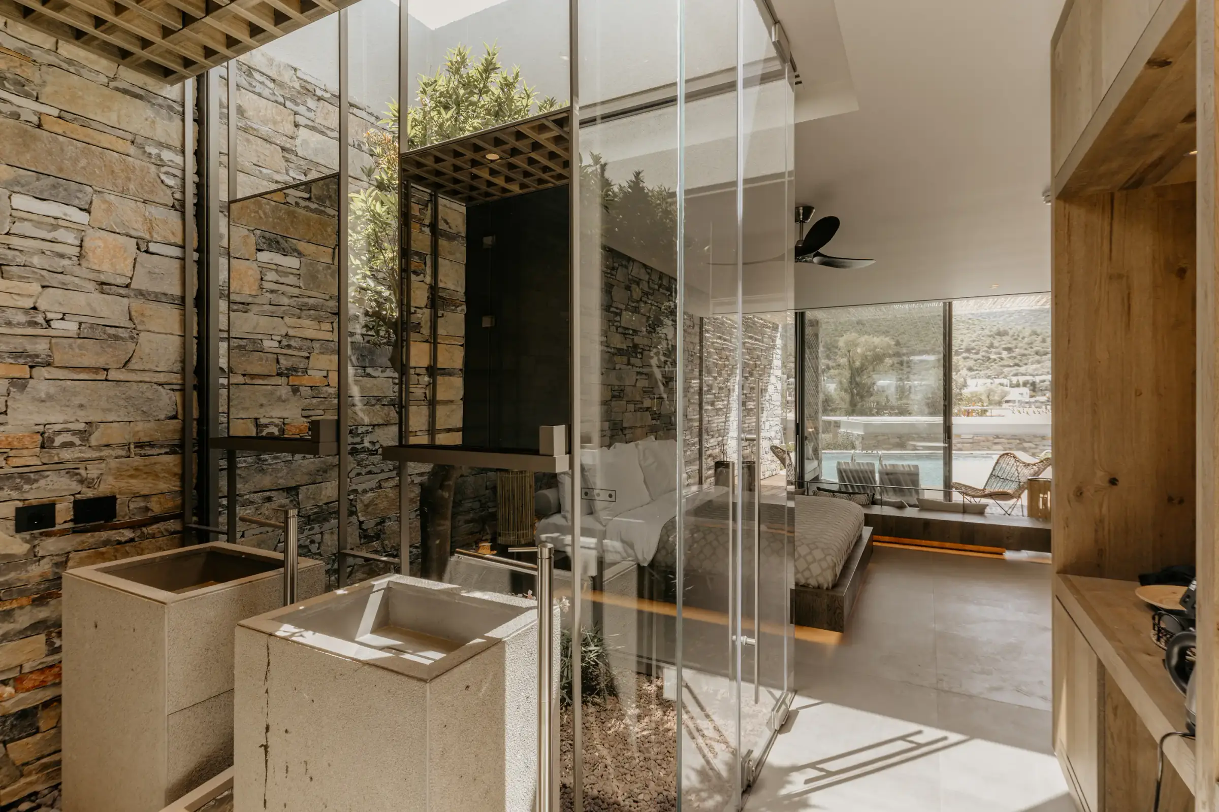 Glass-partitioned bathroom with stone wall and the bedroom beyond