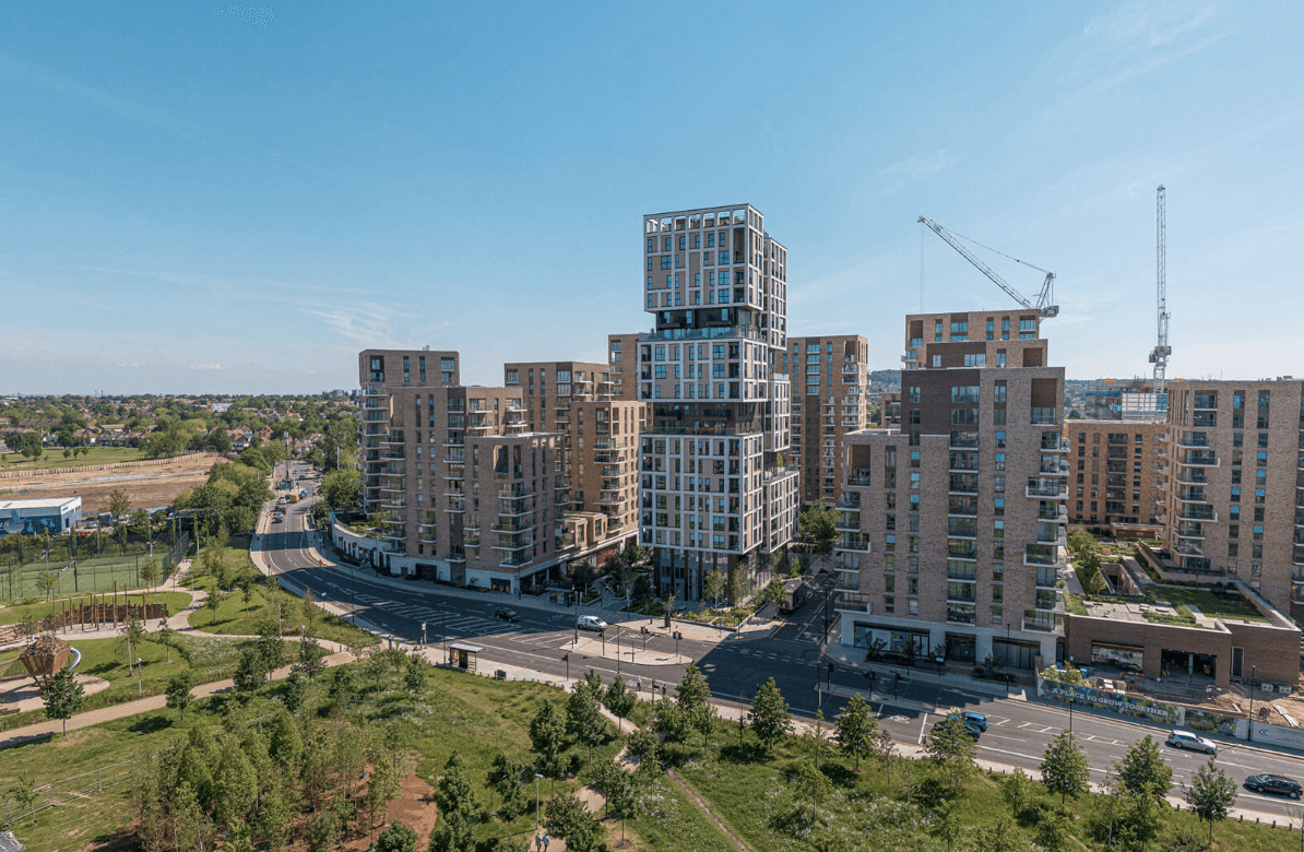 A smiling man with curly hair is sitting at a desk, looking at the camera, with a laptop and a lamp in the background.