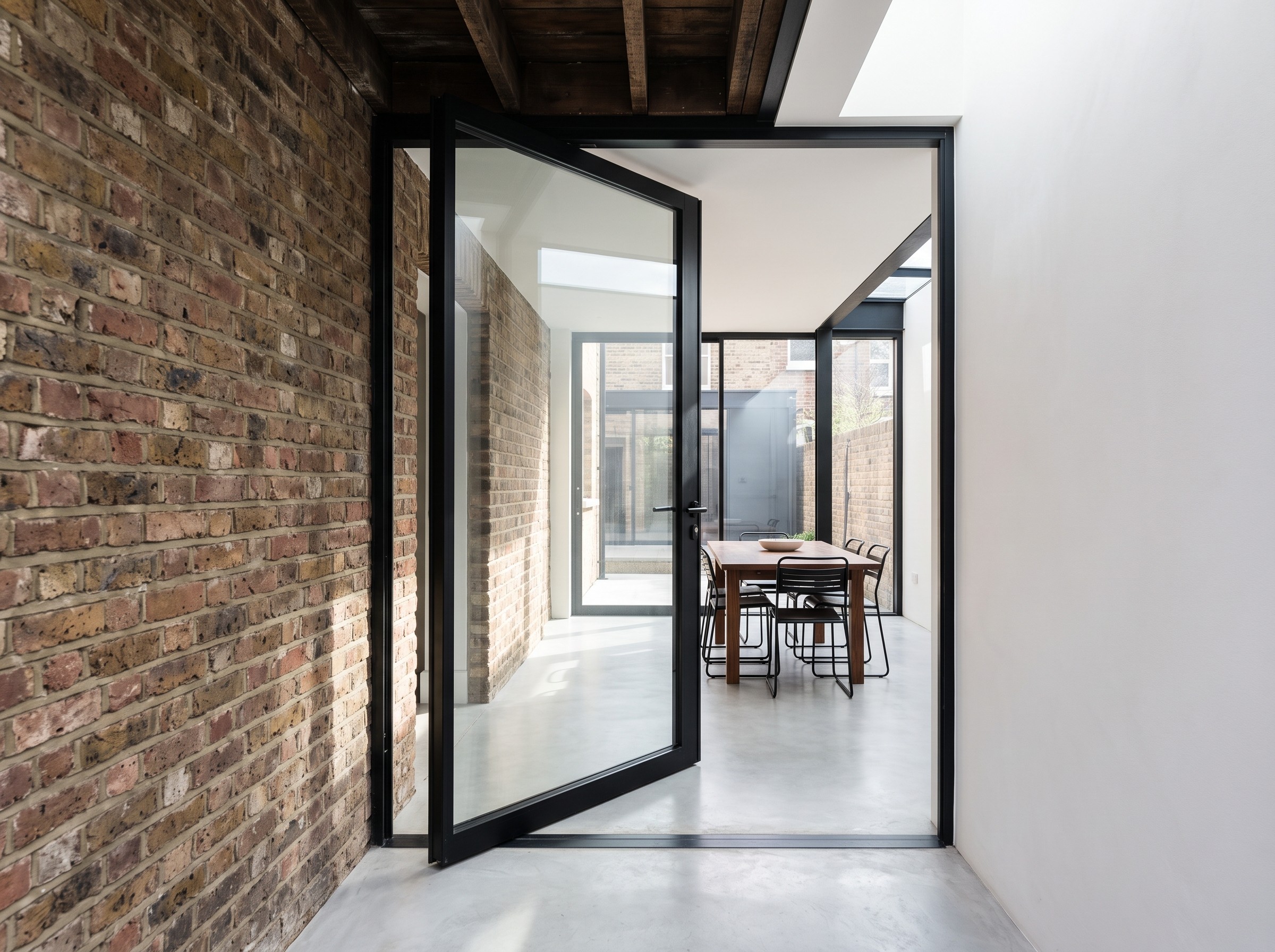 A black pivot door where old brick meets the white rendered side return.