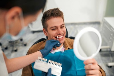 Patient smiling while choosing veneer shade with dentist's assistance.