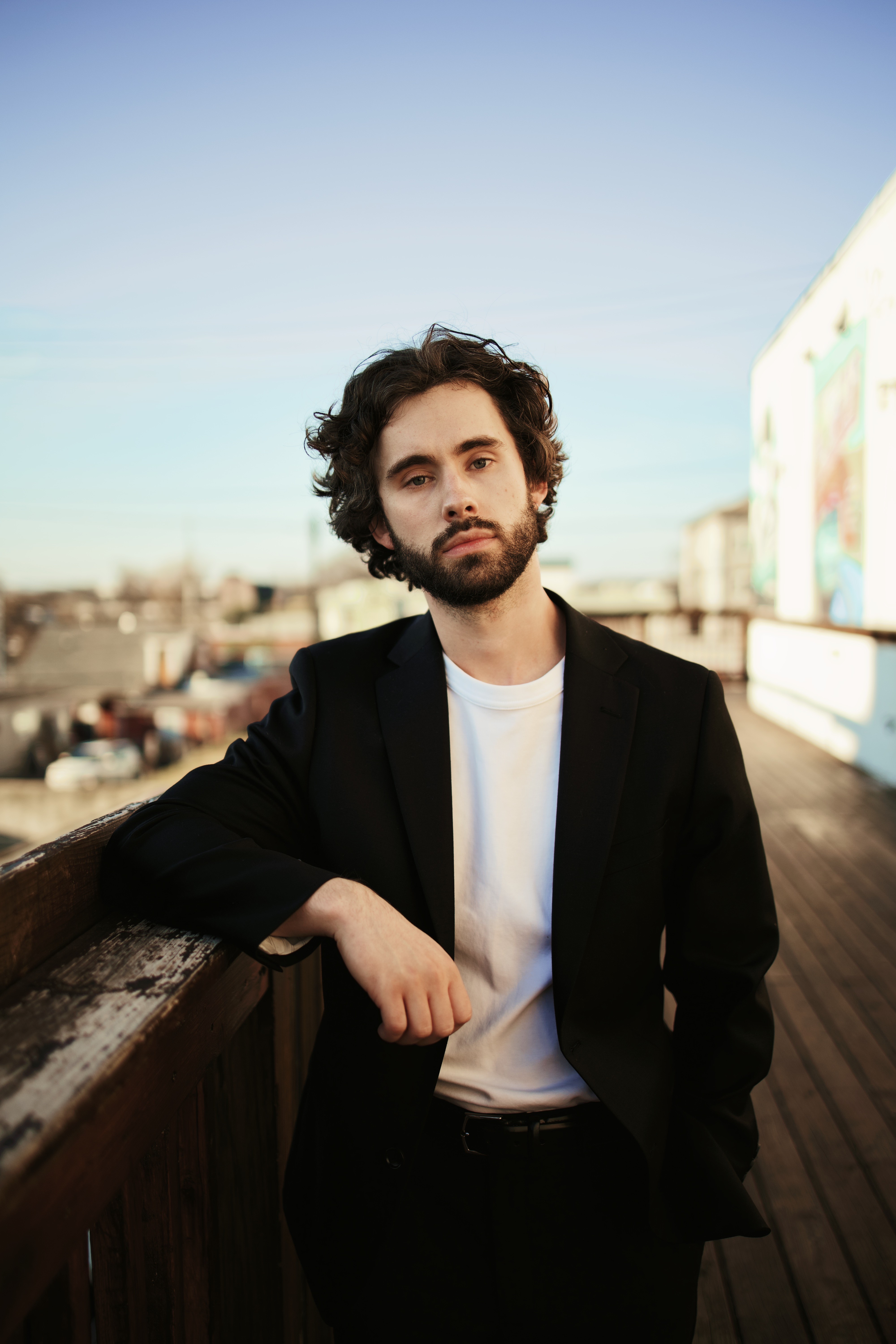 Close-up portrait of a person wearing a gray insulated hooded jacket with the hood up, showing their face framed by the hood against a light background.