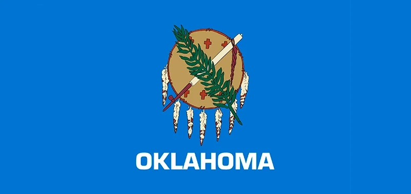 Flag of Oklahoma featuring a brown shield adorned with feathers, a calumet, and olive branch on a blue background. "Oklahoma" is written below.