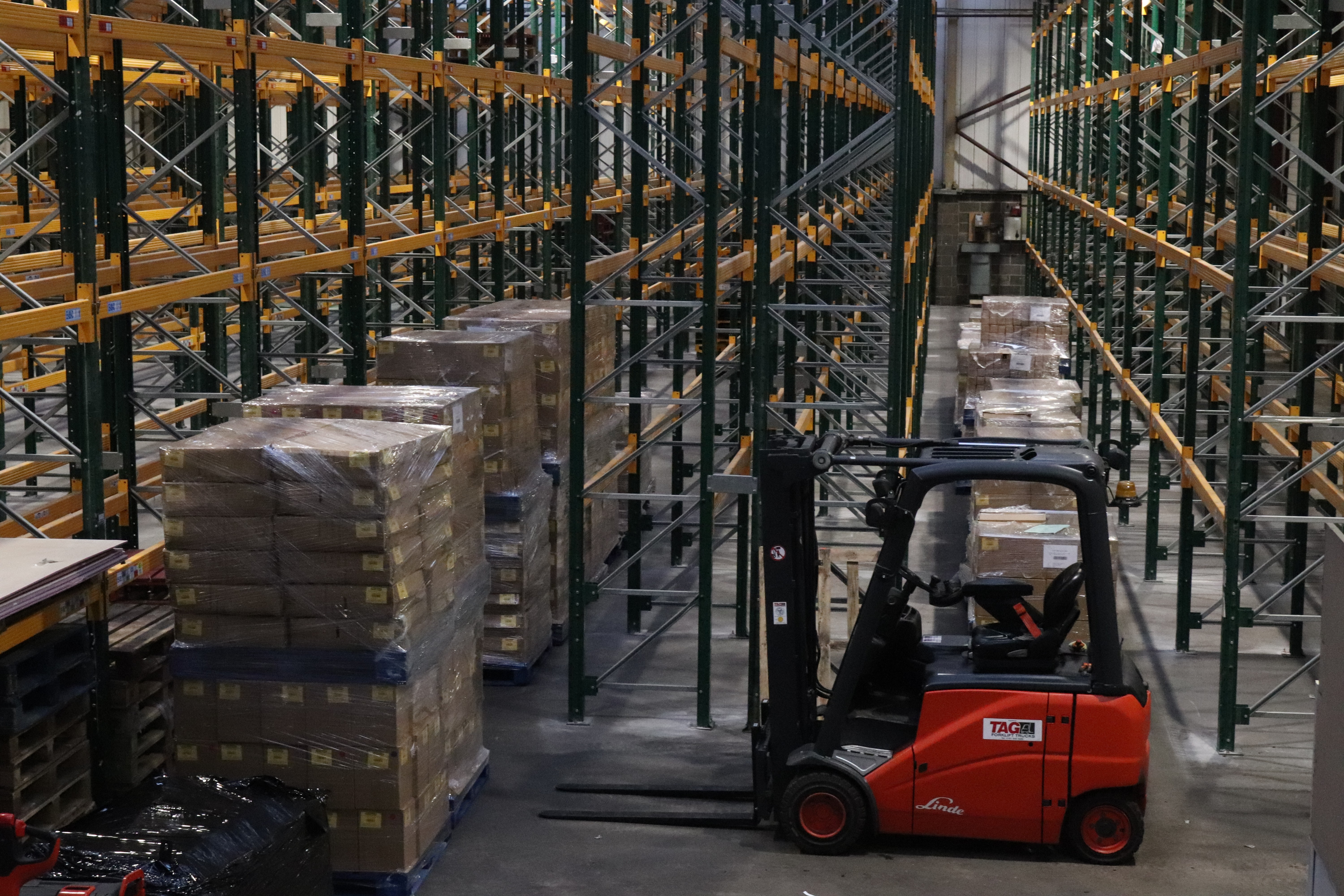 image of a warehouse with racking a forklift and pallets all waiting to be moved