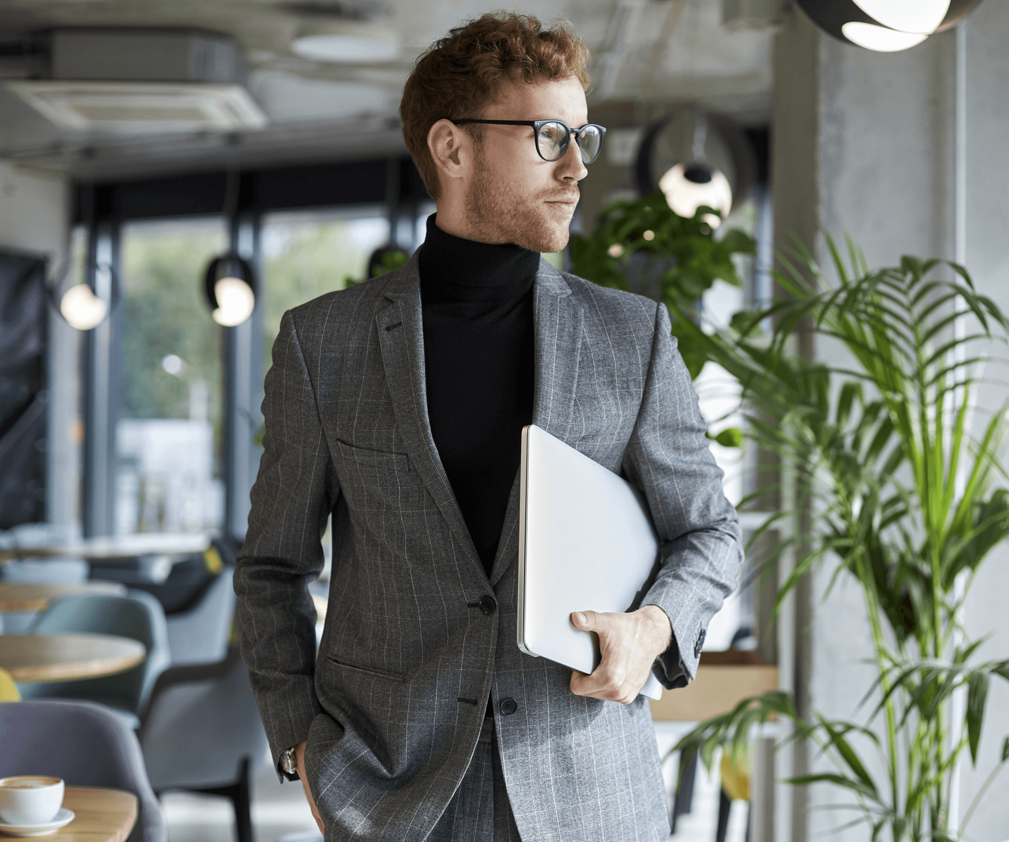 A caucasian man wearing a grey suit walking with a laptop under his arms