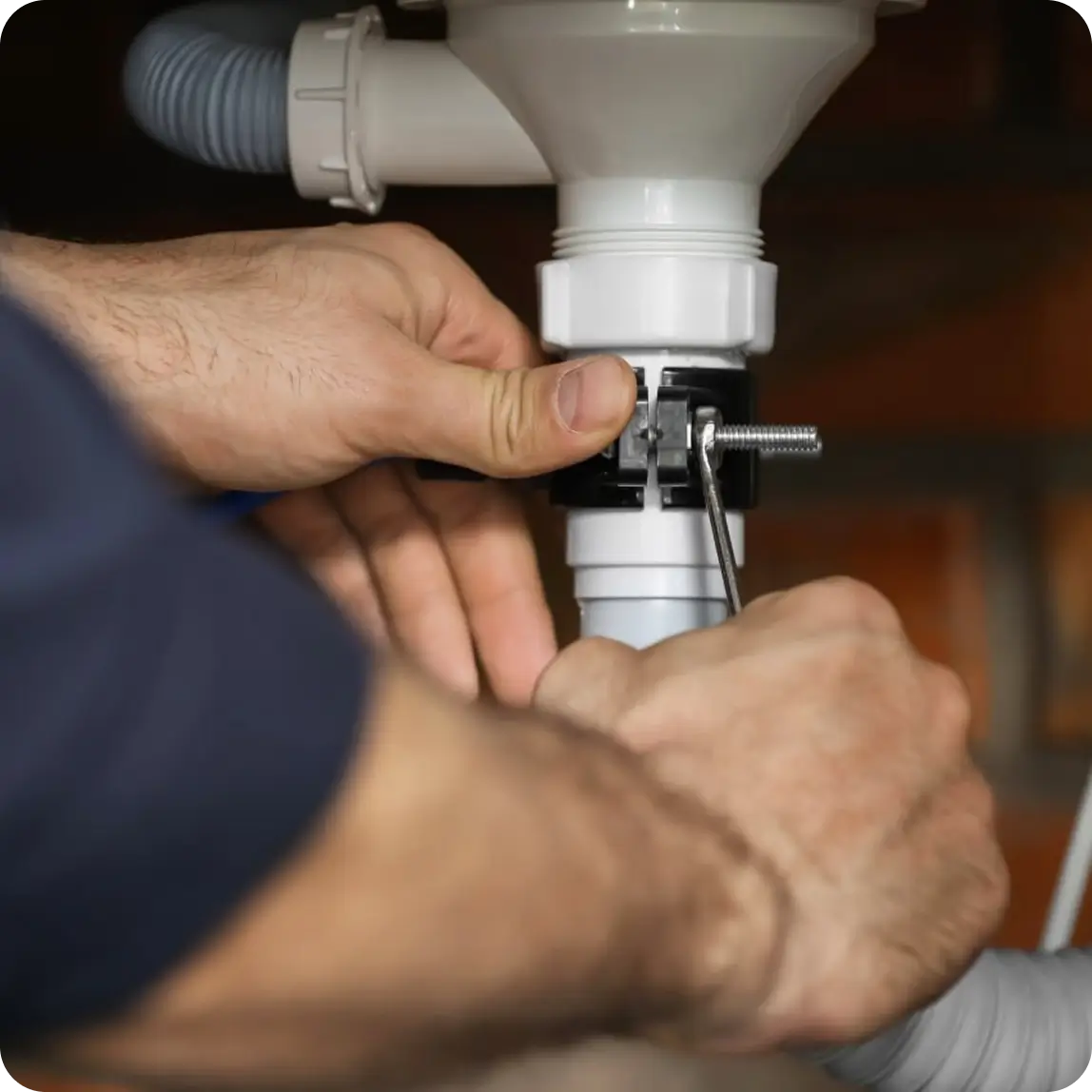 Close-up of a plumber's hands tightening a white drain pipe fitting under a sink