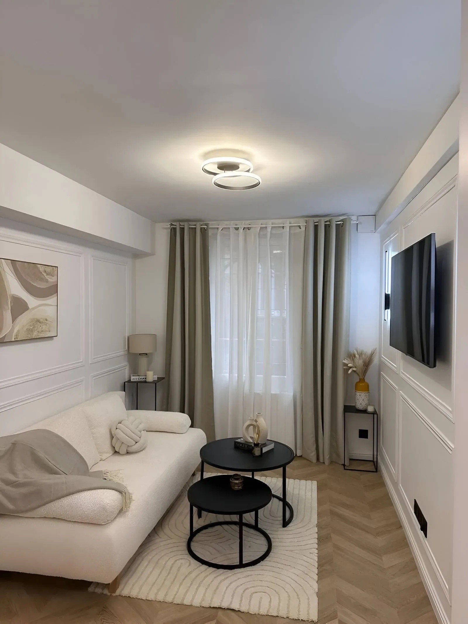 Petit espace de vie optimisé et lumineux avec rideaux beiges, parquet clair et décoration minimaliste élégante.