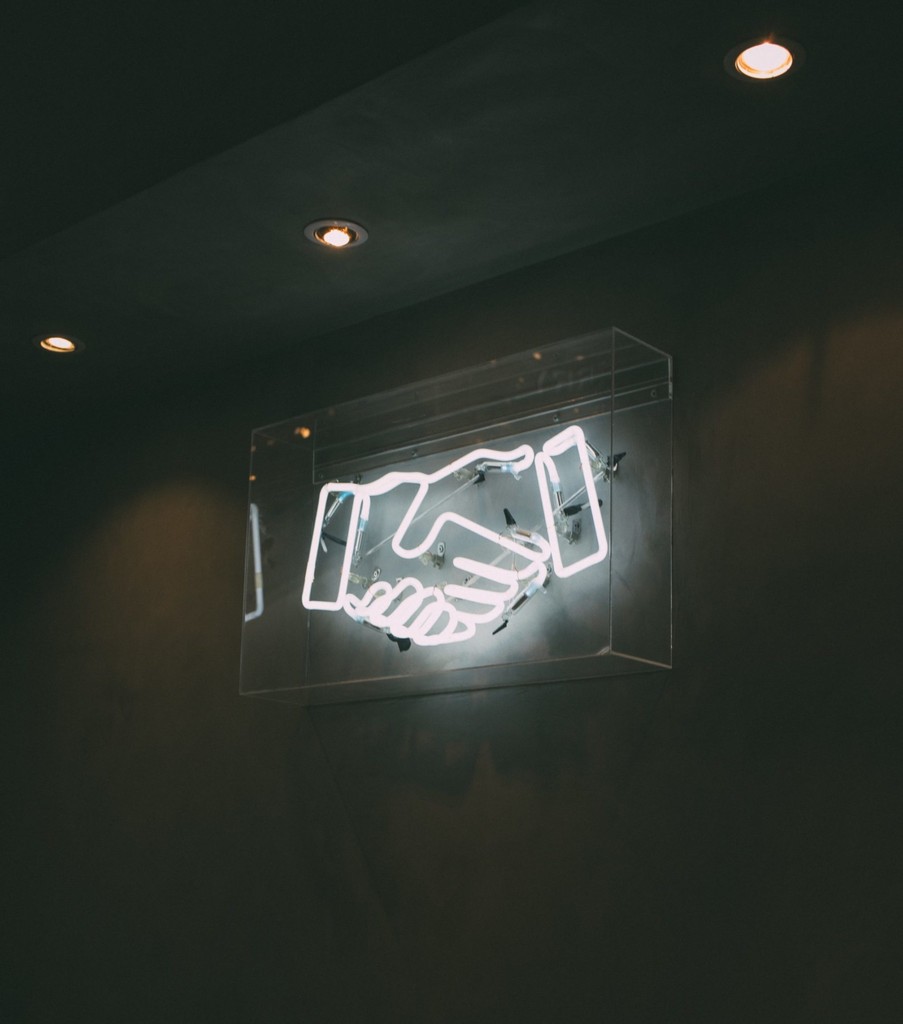 Neon handshake sign on dark wall, symbolizing business partnership.
