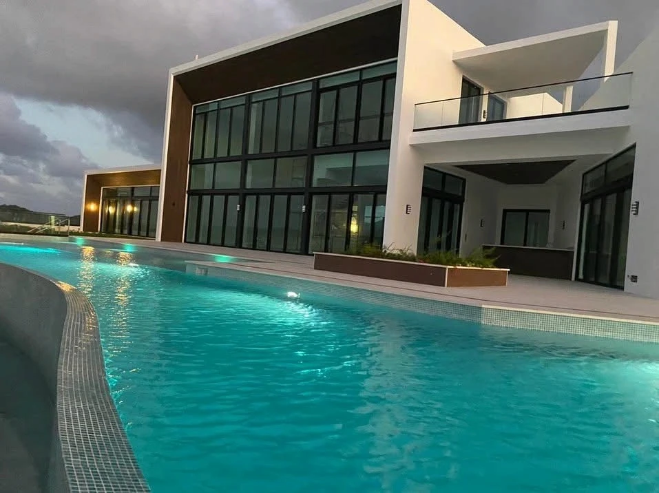 Evening view of The Hill Residence in St. Lucia designed by Atelier International, with illuminated pool, glass curtain wall, and cantilevered upper terrace.