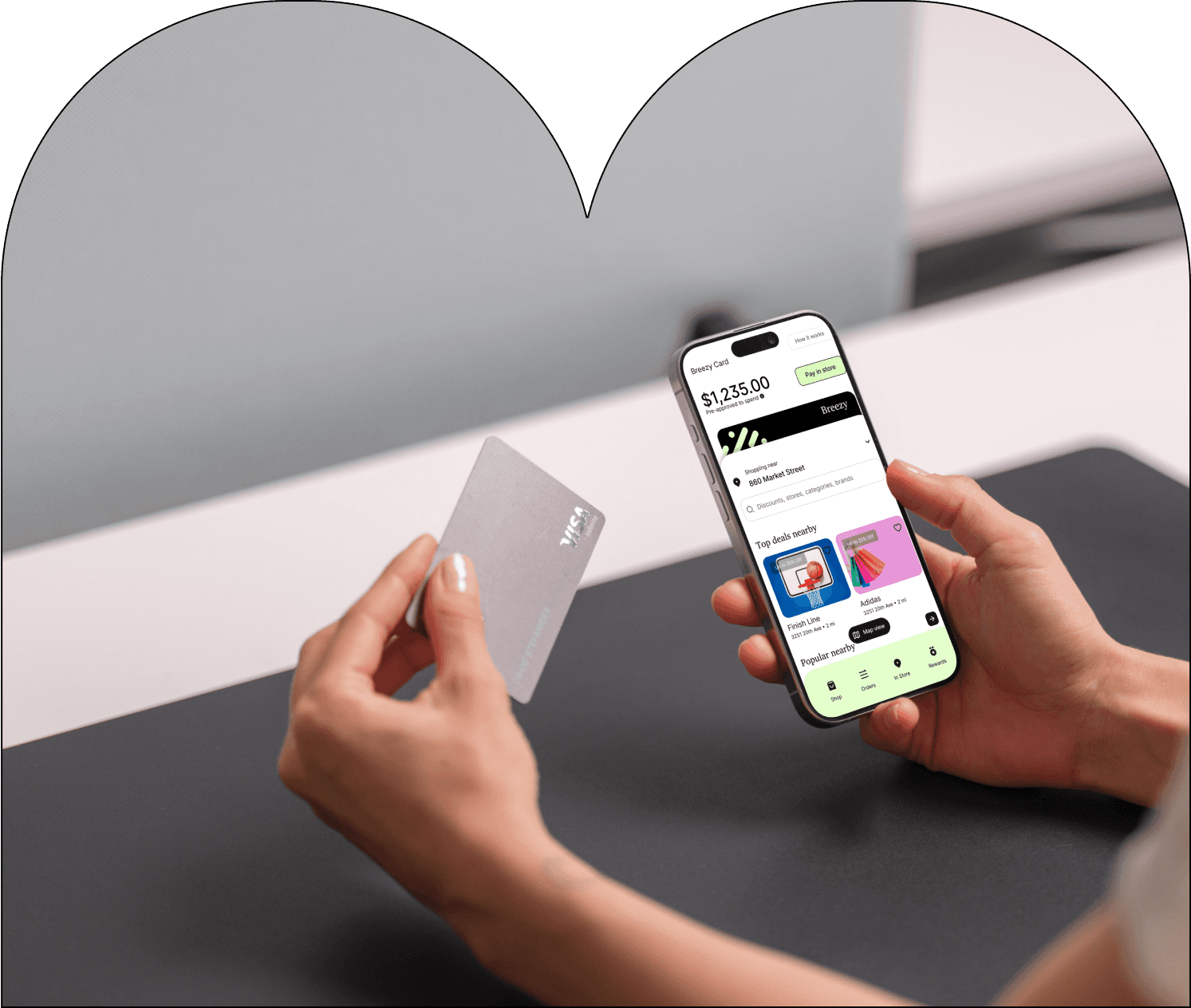 A close-up of a hand holding a credit card in front of a laptop, with another hand using a smartphone displaying a financial app. The app screen shows a digital Breezy card with a balance of $16,058.94, highlighting the availability of both physical and digital cards for seamless transactions.