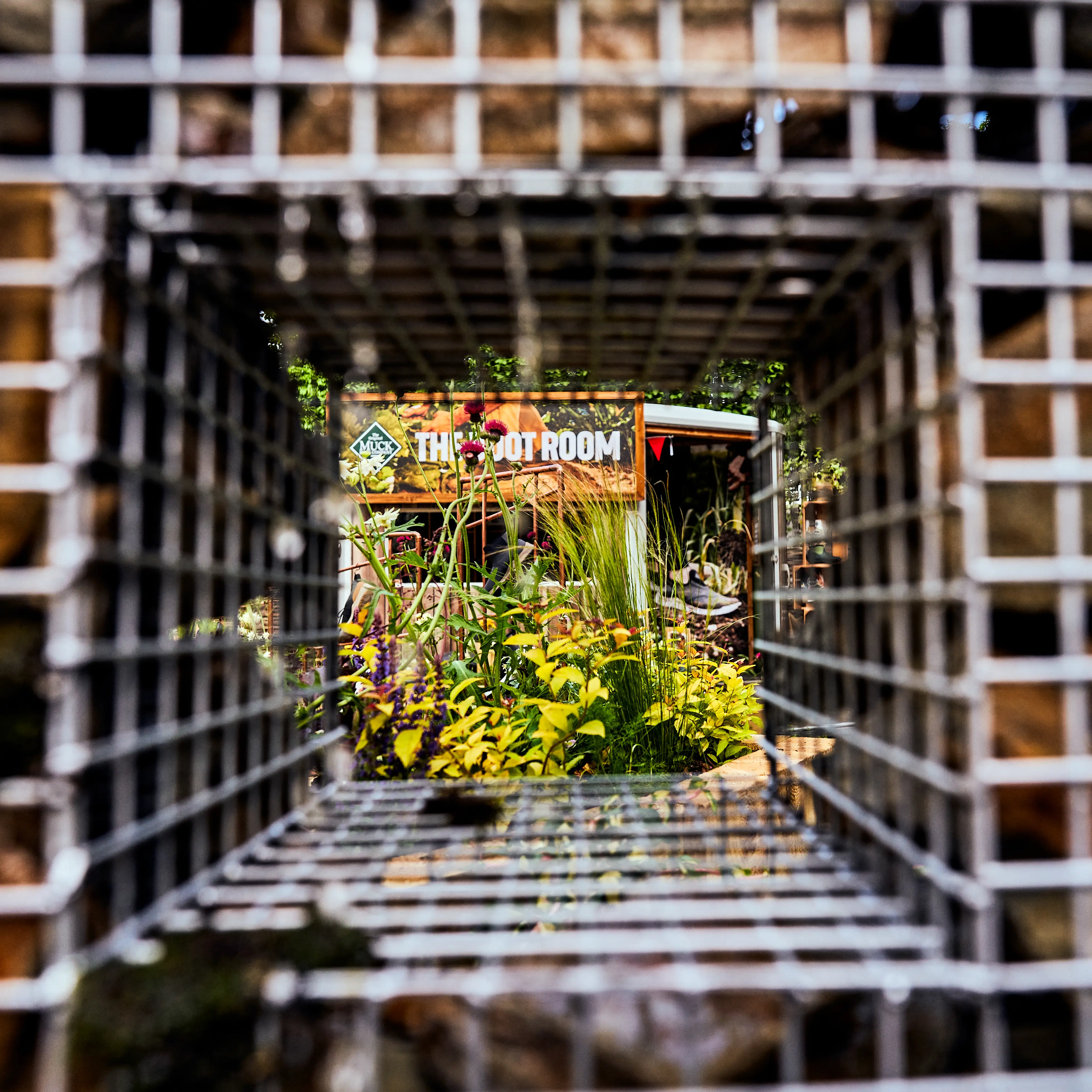 View through a square wire grid, framed by greenery and wooden structures in the background.
