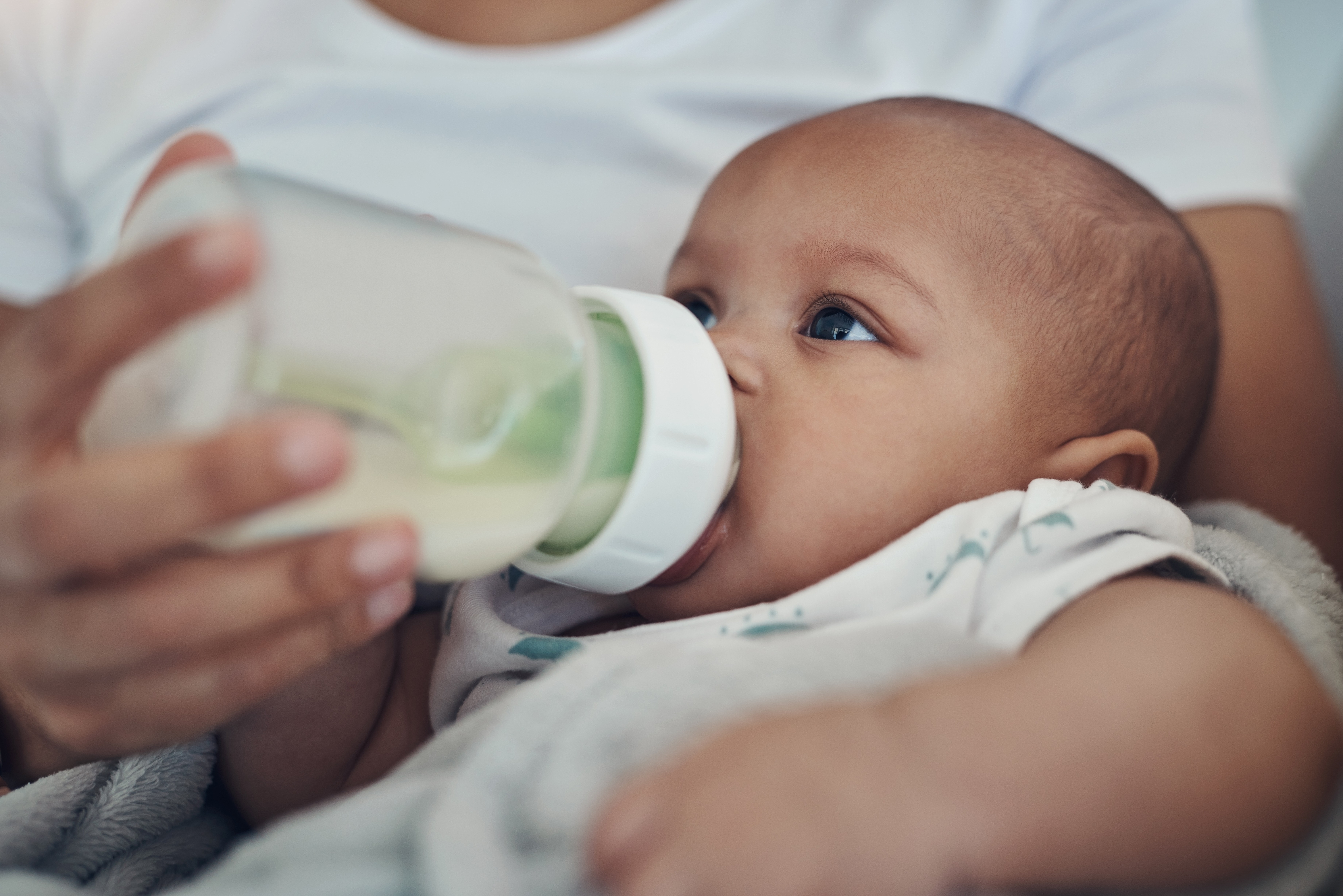 Close-up of a baby being bottle-fed milk while cradled in an adult's arms