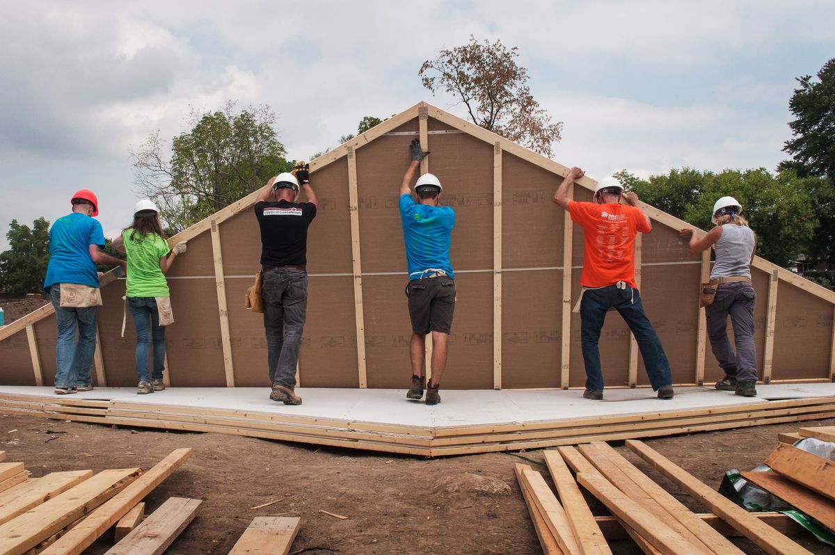 Smiling young man with short hair poses against a dark background, wearing a green button-up shirt.