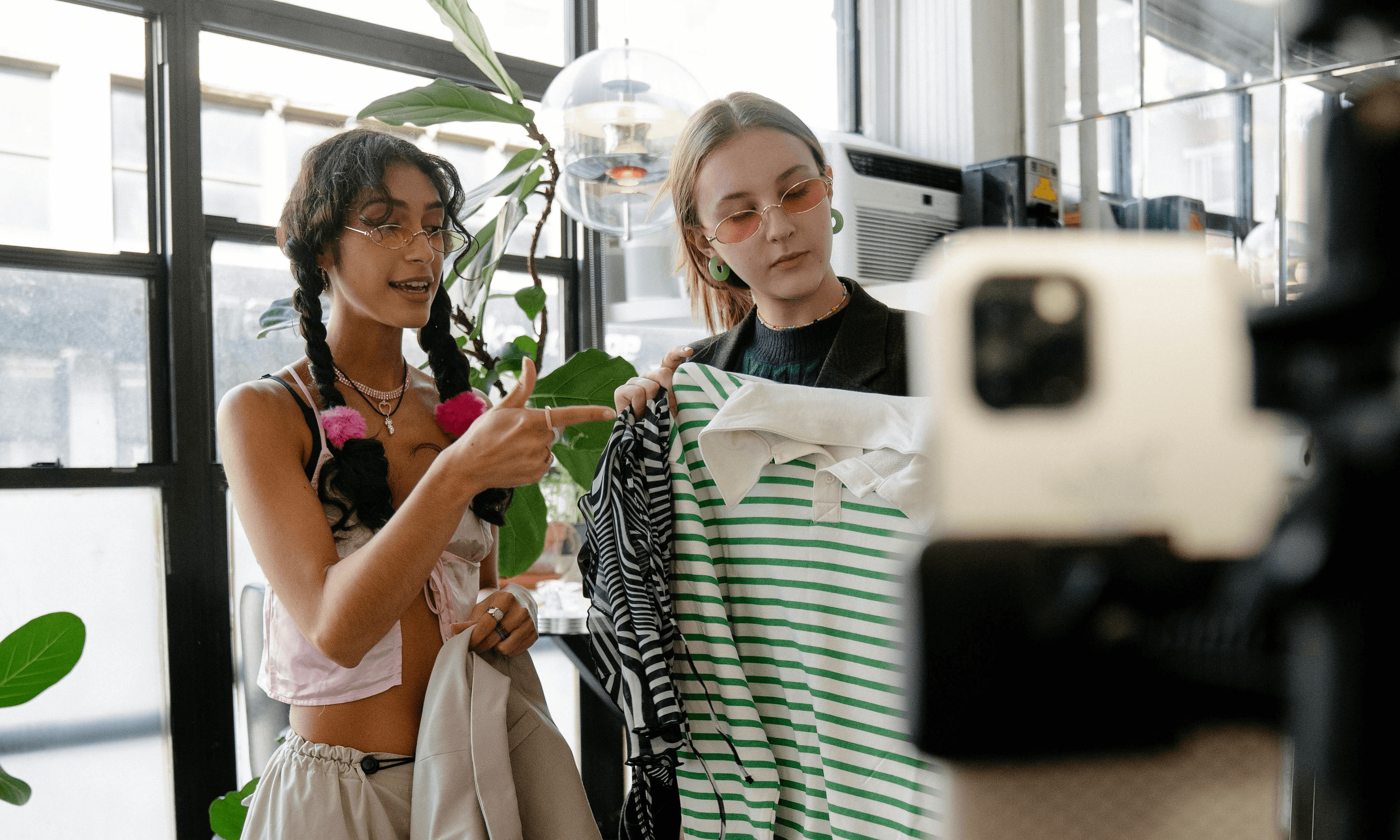 Two Influencer hold up clothing while smiling at a camera while making content