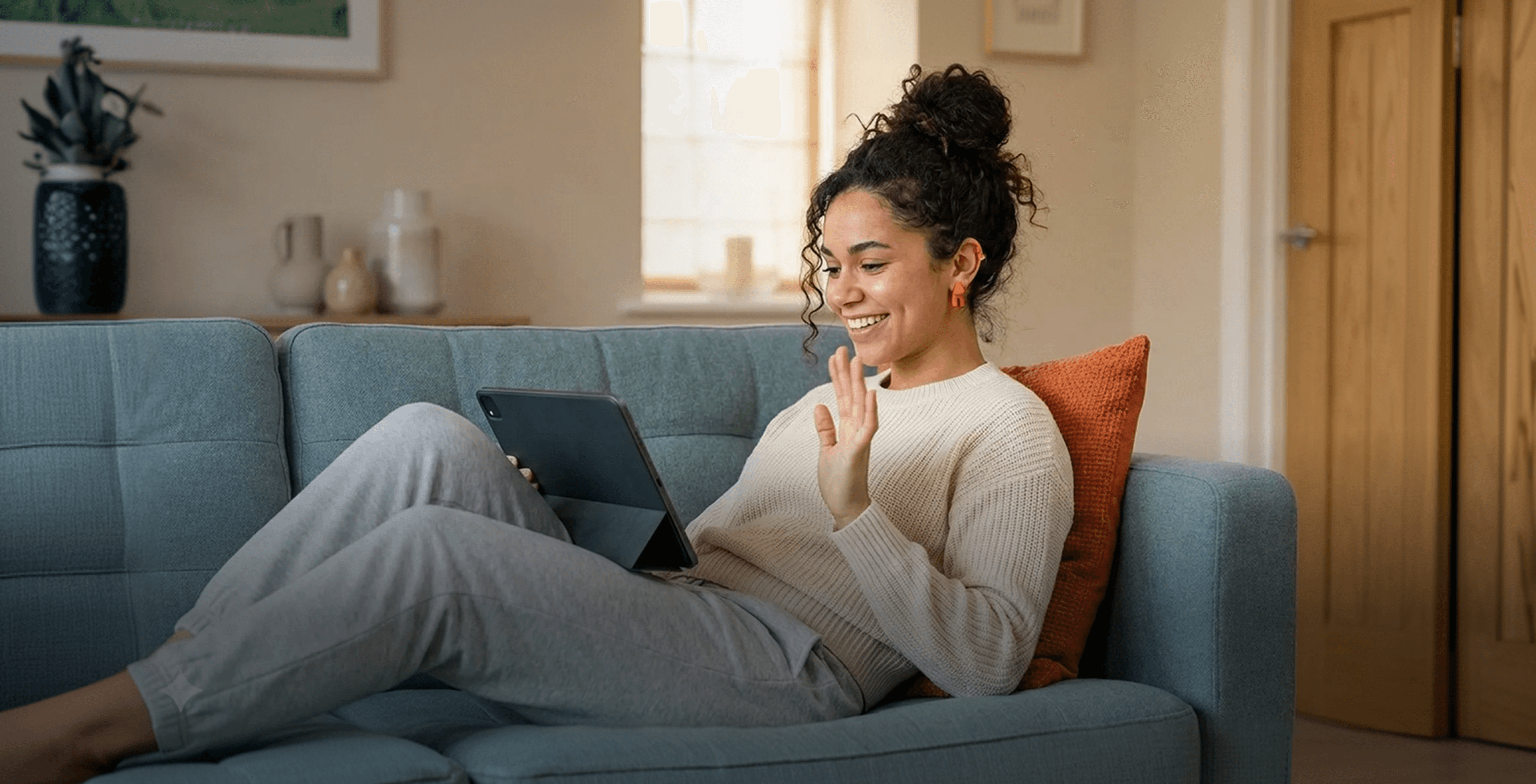 Mulher sentada no sofá fazendo uma videochamada usando um tablet