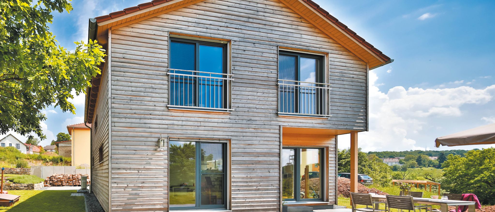Holzhausfassade mit horizontalen Holzverschalungen, mehreren Fenstern, kleinen Balkonen und Unterdach aus Holz.