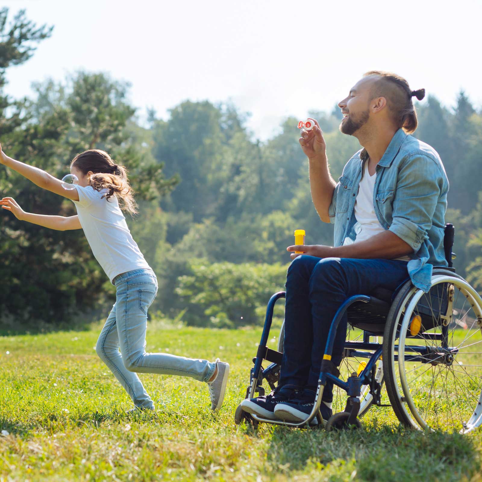 middle aged man with paraplegia in a wheelchair laughing with his daughter in a field