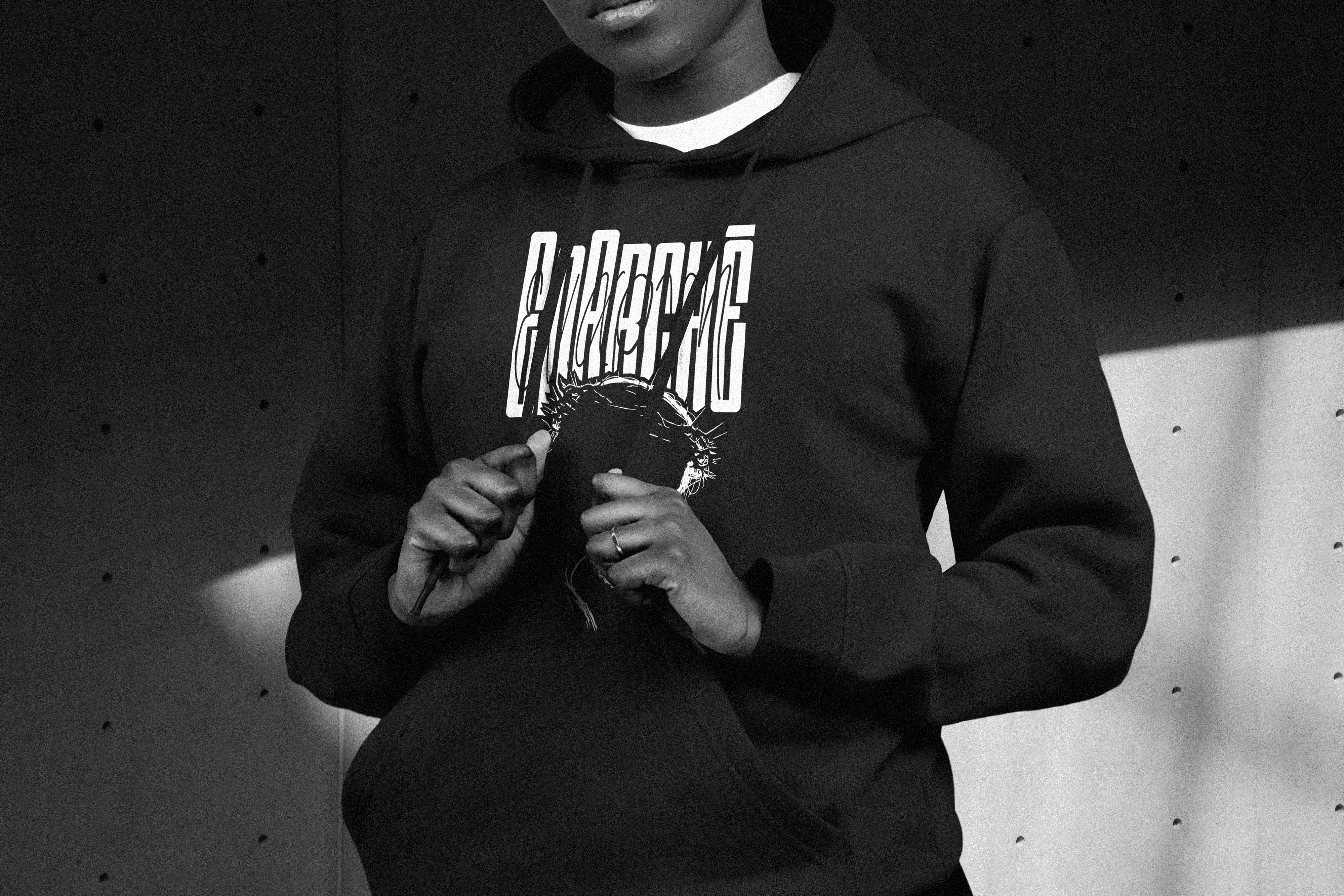 Young woman wearing a black EnArchē branded hoodie.