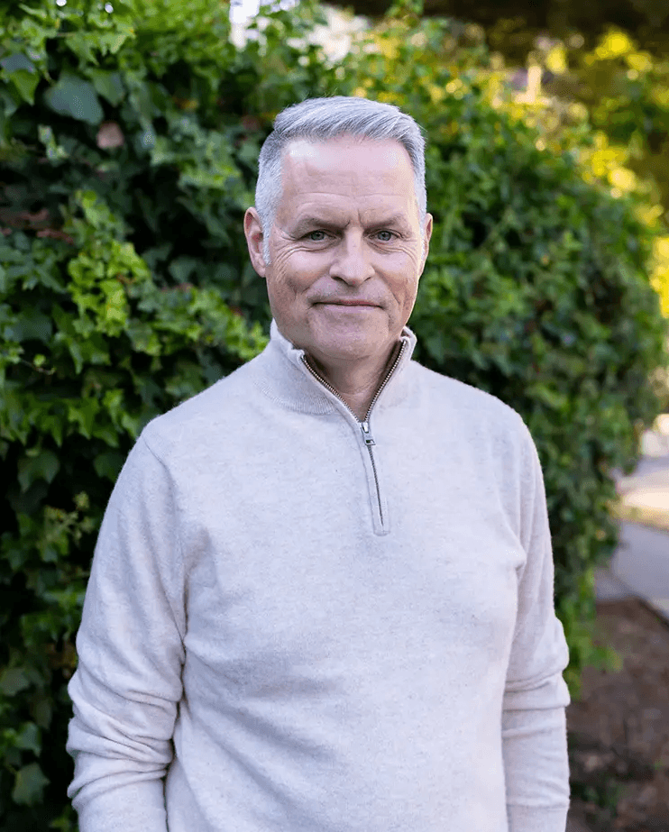 John Coyne, PsyD, a CBT-I therapist treating chronic insomnia in Marin County and online in California, is gently smiling at the camera in front of a lush, green hedge