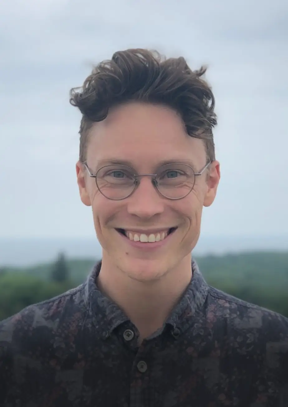 A smiling young men with a green landscape background