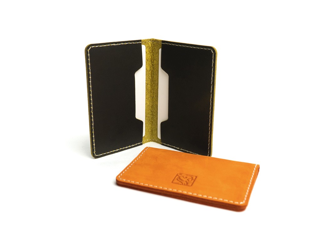 A black leather card holder standing open to show the two interior pockets, next to a closed orange one lying flat.