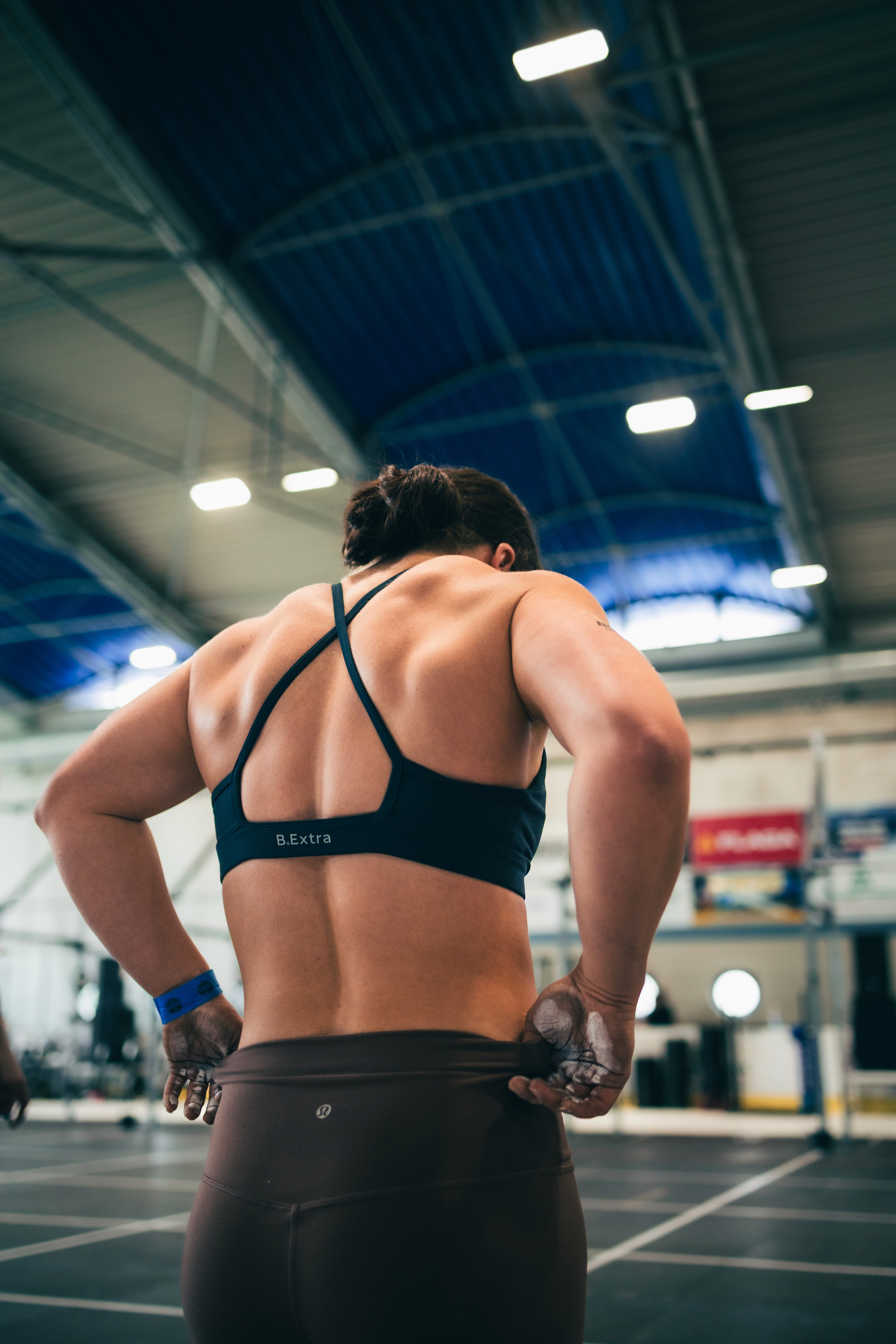 An athlete in a black strappy sports bra seen from behind beneath the competition hall’s roof.