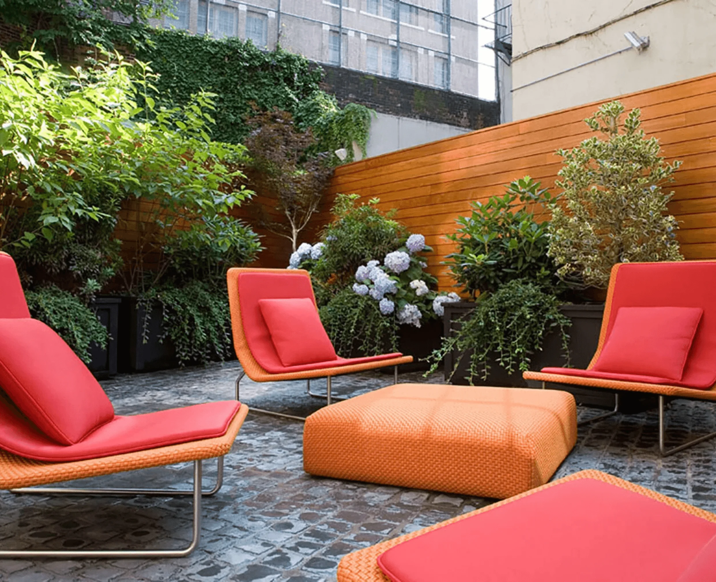 Red woven lounge chairs and an ottoman furnish a plant-filled outdoor courtyard