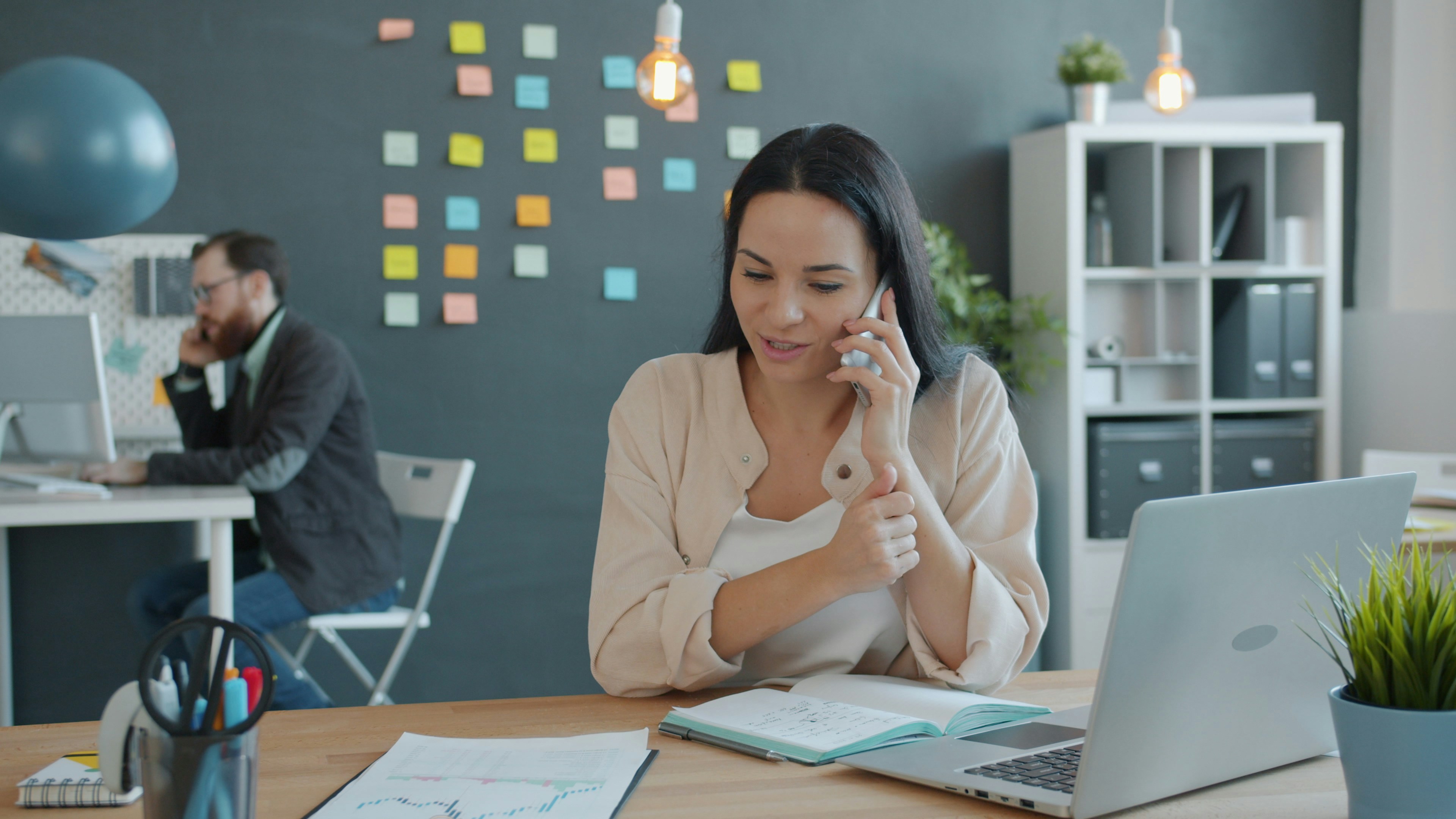 Woman talking on phone at desk with laptop.