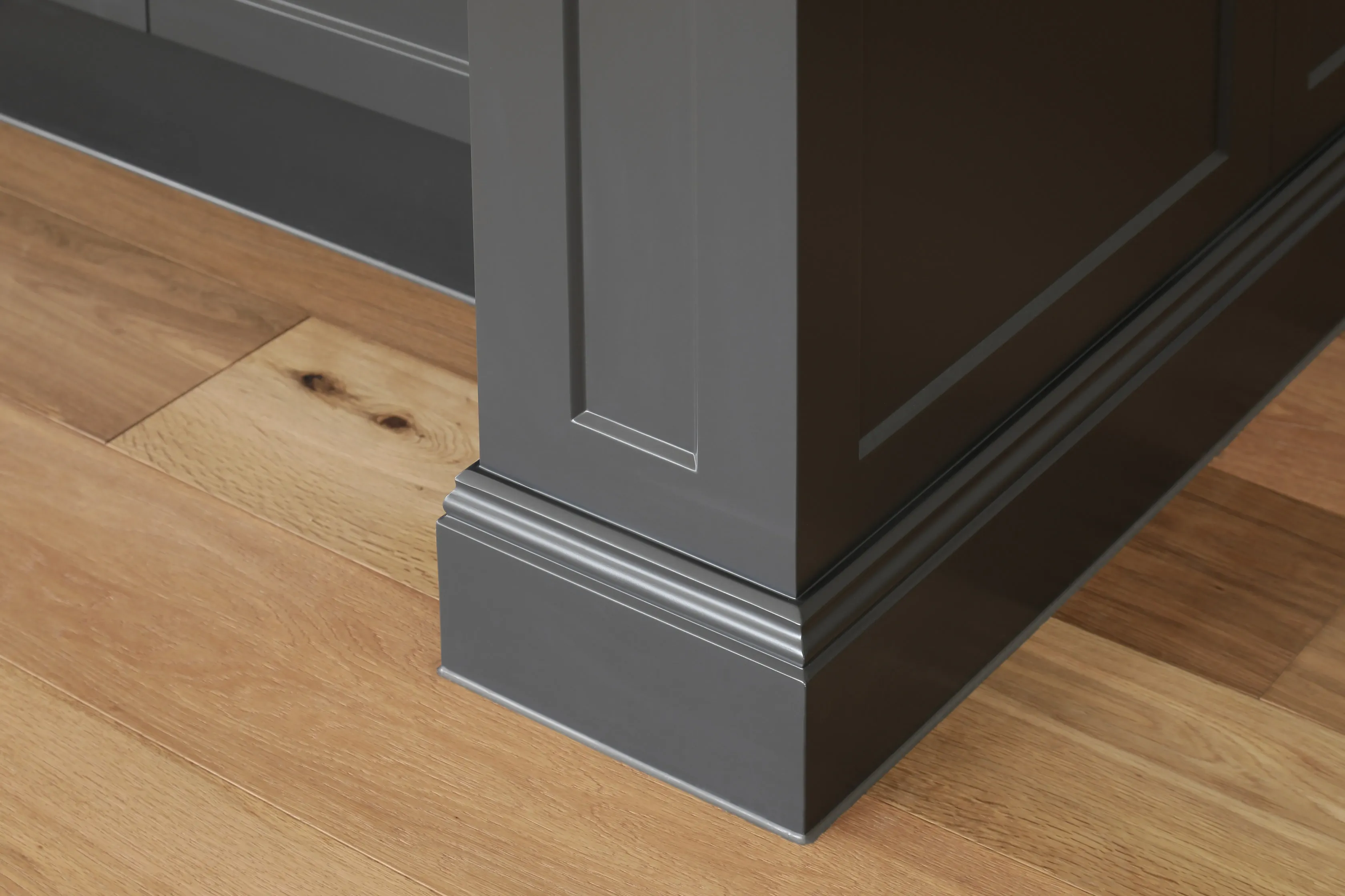 Close-up of the charcoal shaker kitchen island base with classical plinth moulding against oak herringbone floors