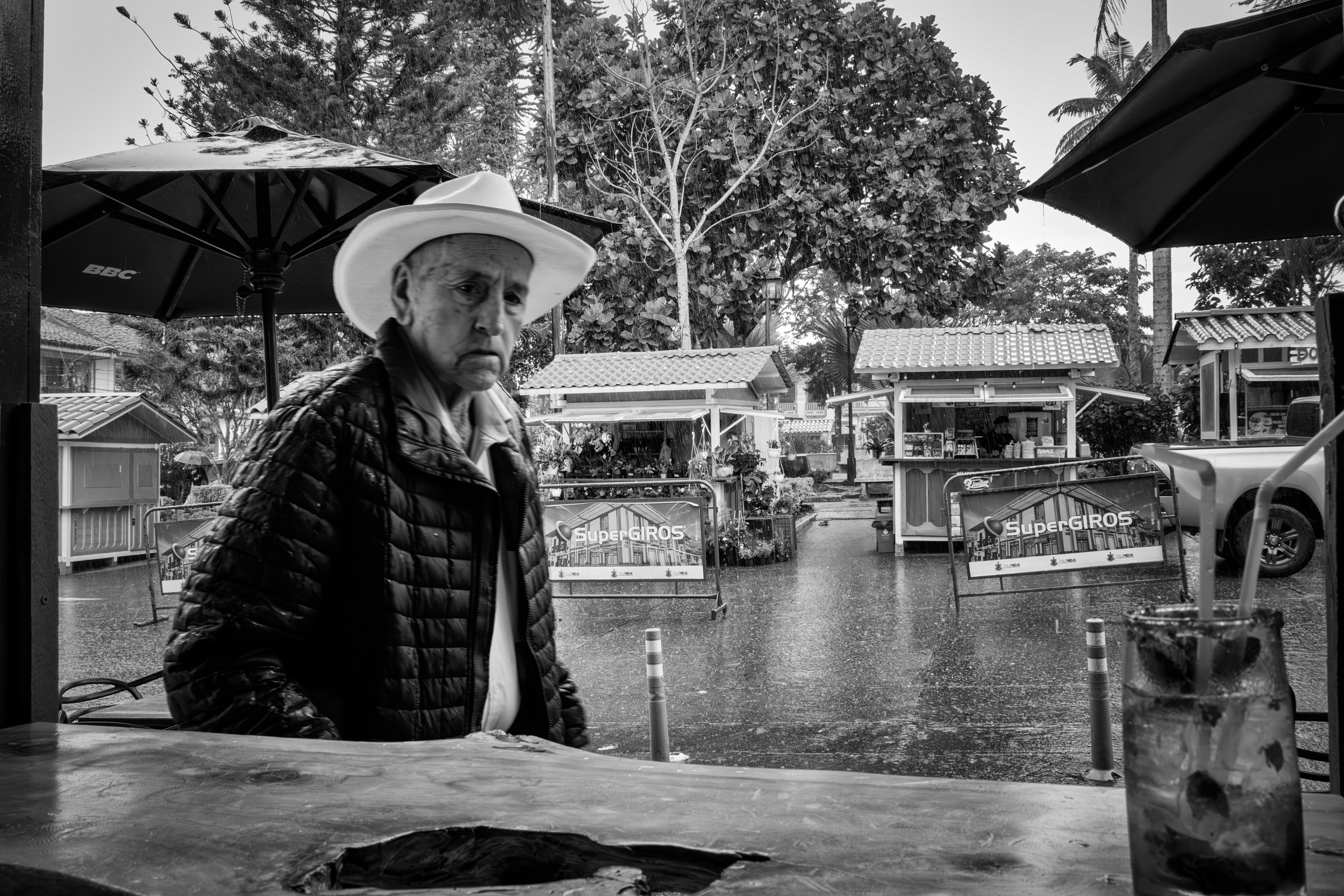 Rainy street scene with people passing by a bar window.