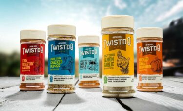 Jars of five different Twist'd Q seasonings backlit against a bright sky.