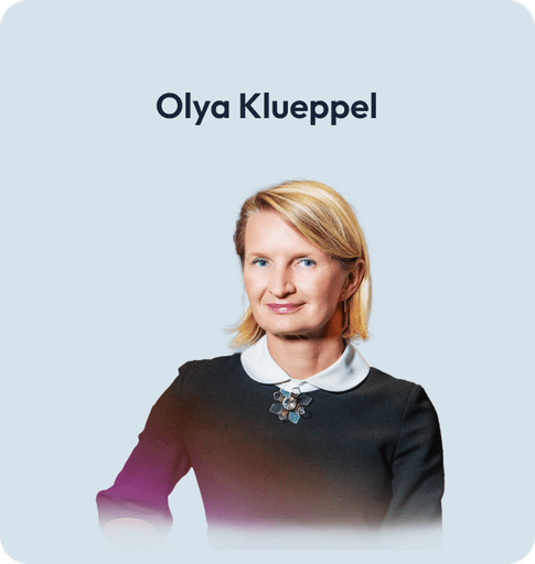 Porträt von Olya Klueppel, professionell lächelnd im dunklen Top und Blazer.