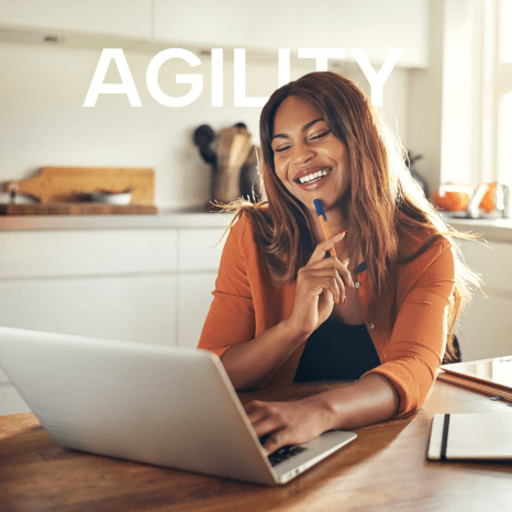 A smiling woman working on a laptop in an office setting, with the word "AGILITY" prominently displayed in the background