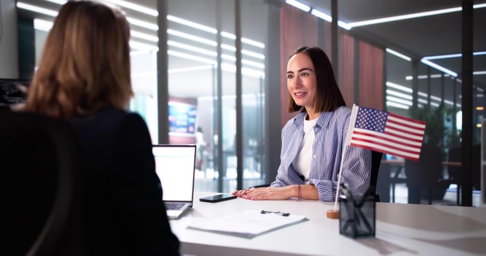A woman sitting at a desk with an American flag displayed prominently on it. Form I539