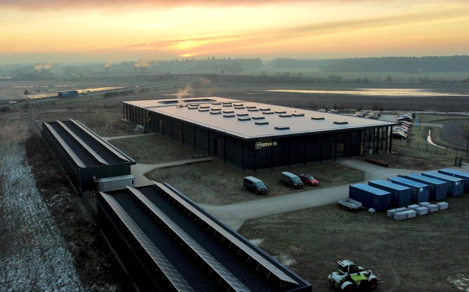 Aerial view of the modern industrial headquarter building with solar panels, parked cars, and containers on a sunny day.