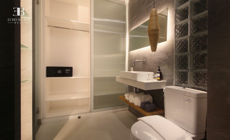 Canggu Bathroom Design: Stylish ensuite with gray stone tiles, vessel sink, and a unique glass block feature wall separating the shower area. Luxury design at Echo Beach Suite, Bali.