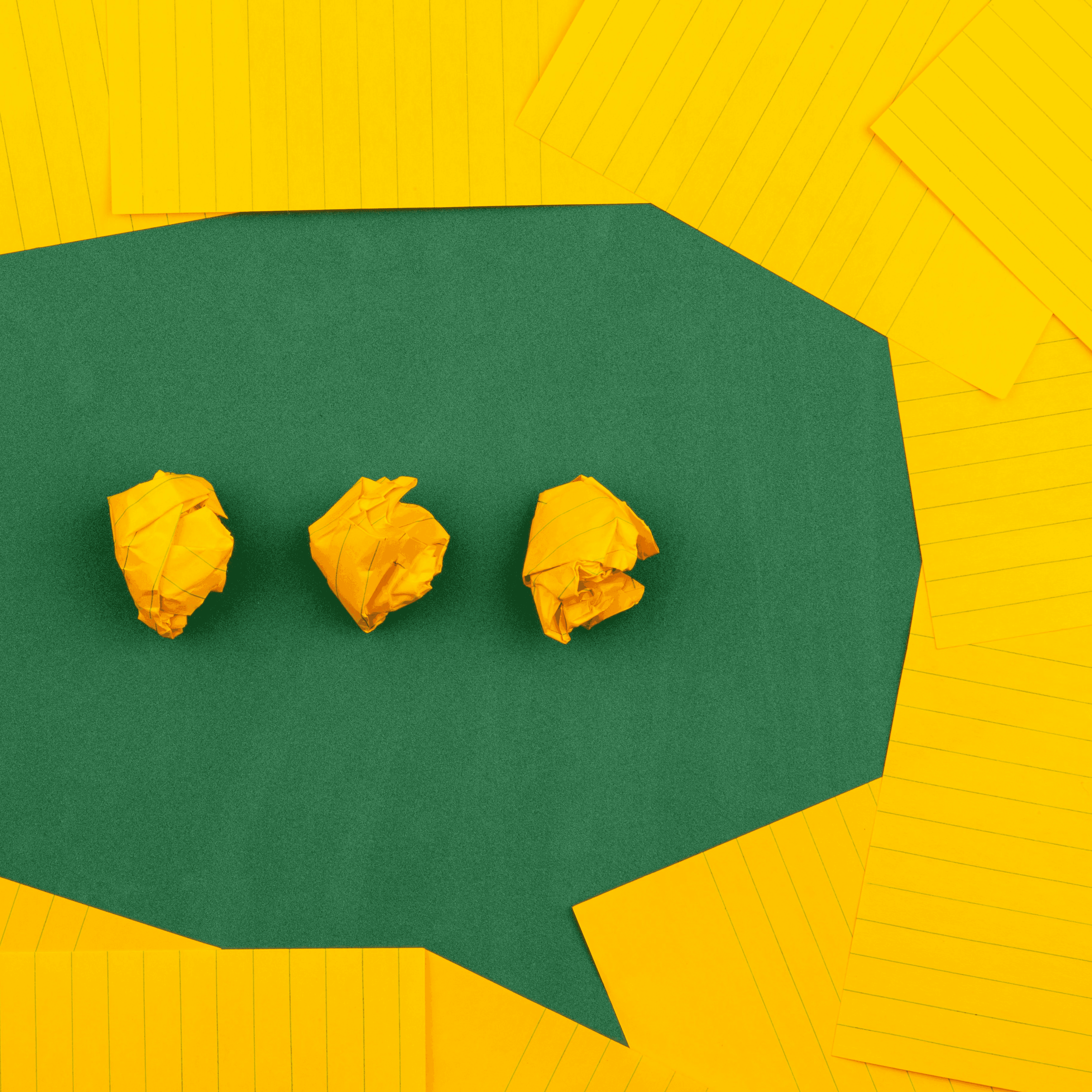 three crumpled yellow papers on green surface surrounded by yellow lined papers