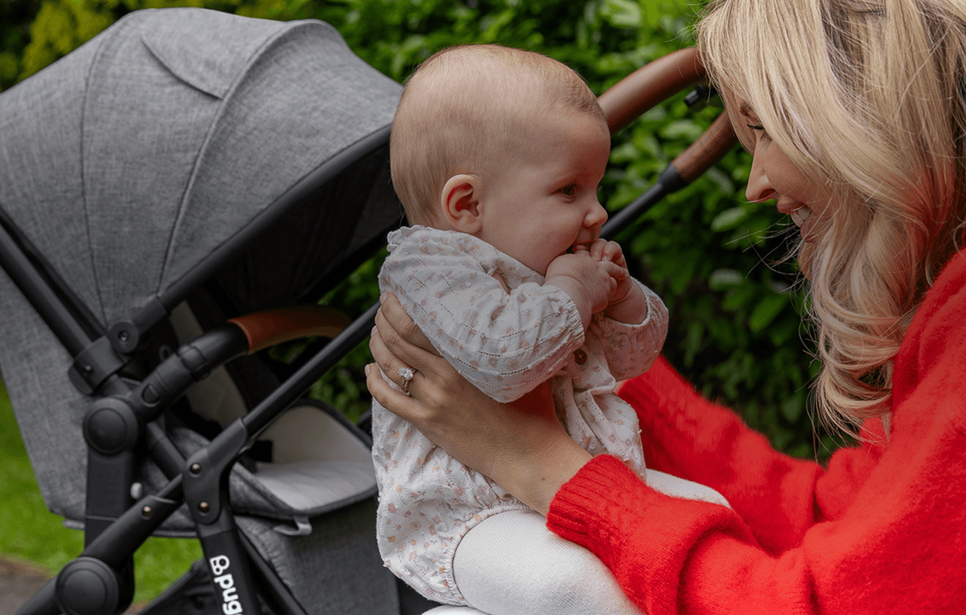 A mum holding her baby next to a buggy in a park