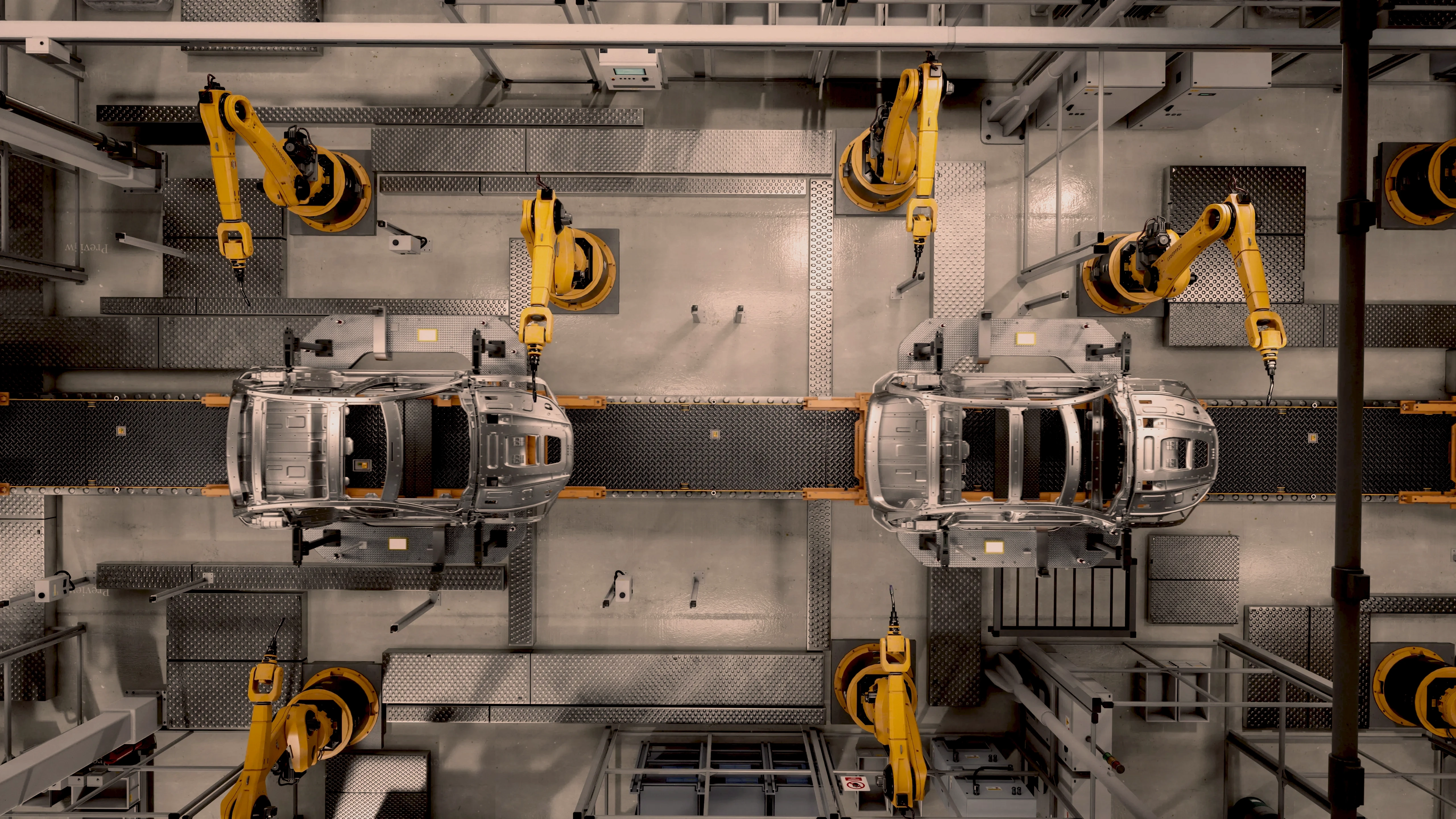 Overhead view of yellow industrial robots working on car bodies along an assembly line