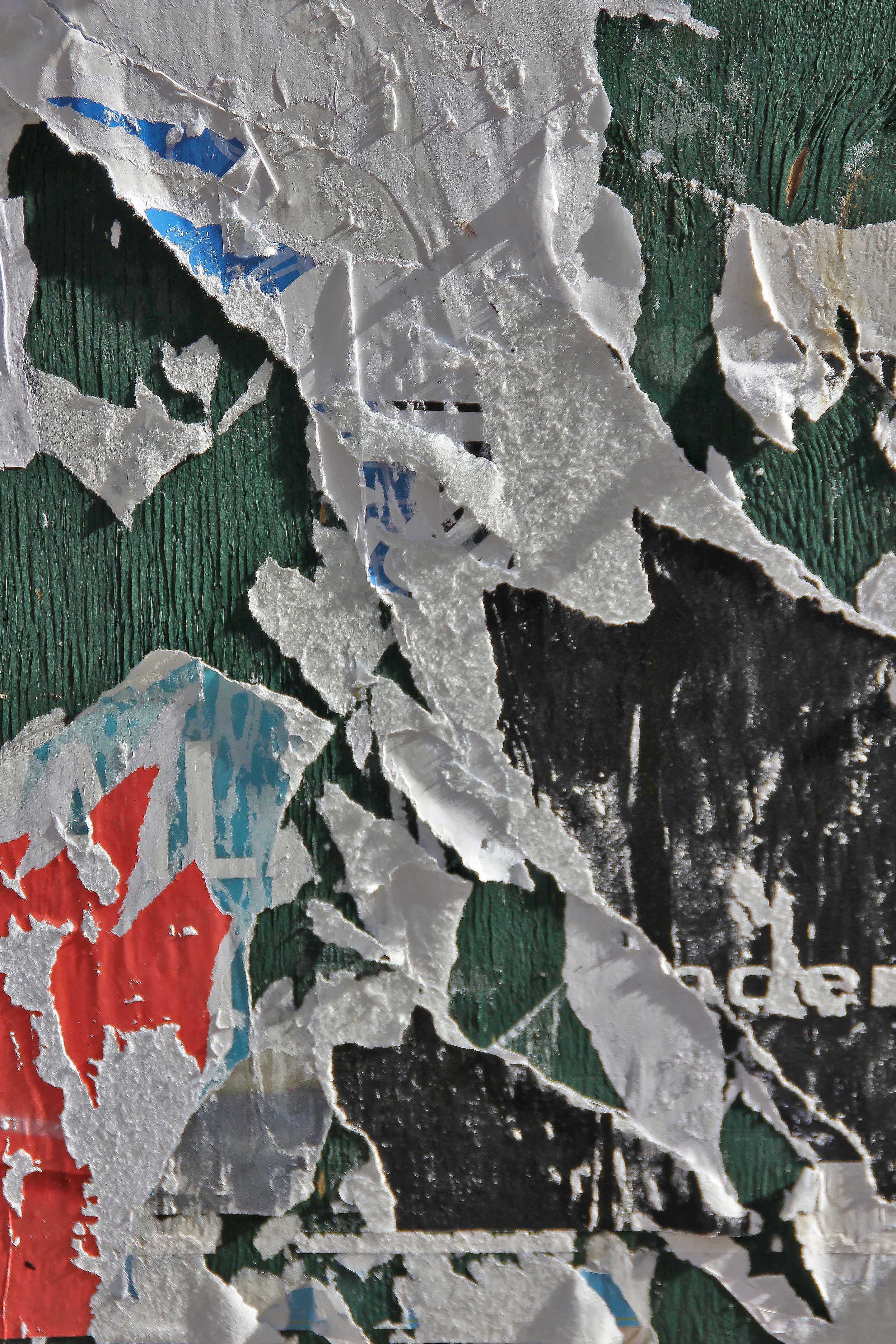 Close-up photograph of layered, peeling posters revealing fragments of color, text, and texture. The torn surfaces expose traces of time and weathering, transforming decay into an abstract composition.