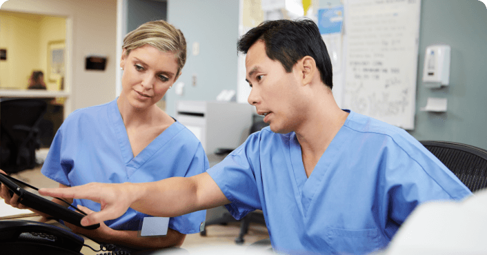 Two healthcare workers reviewing information on a tablet together.