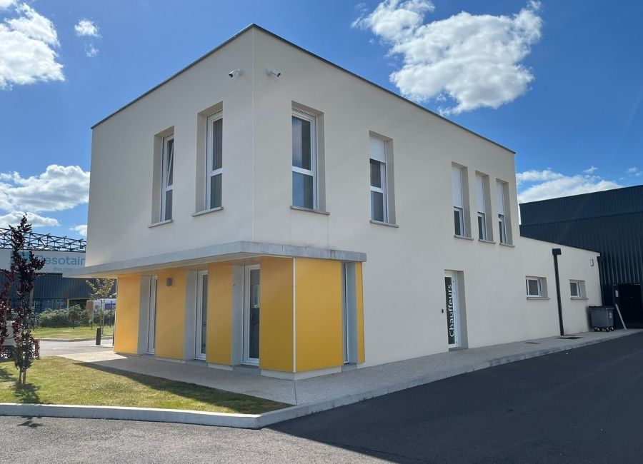 Bâtiment administratif ou annexe avec façade blanche et porte sectionnelle jaune.