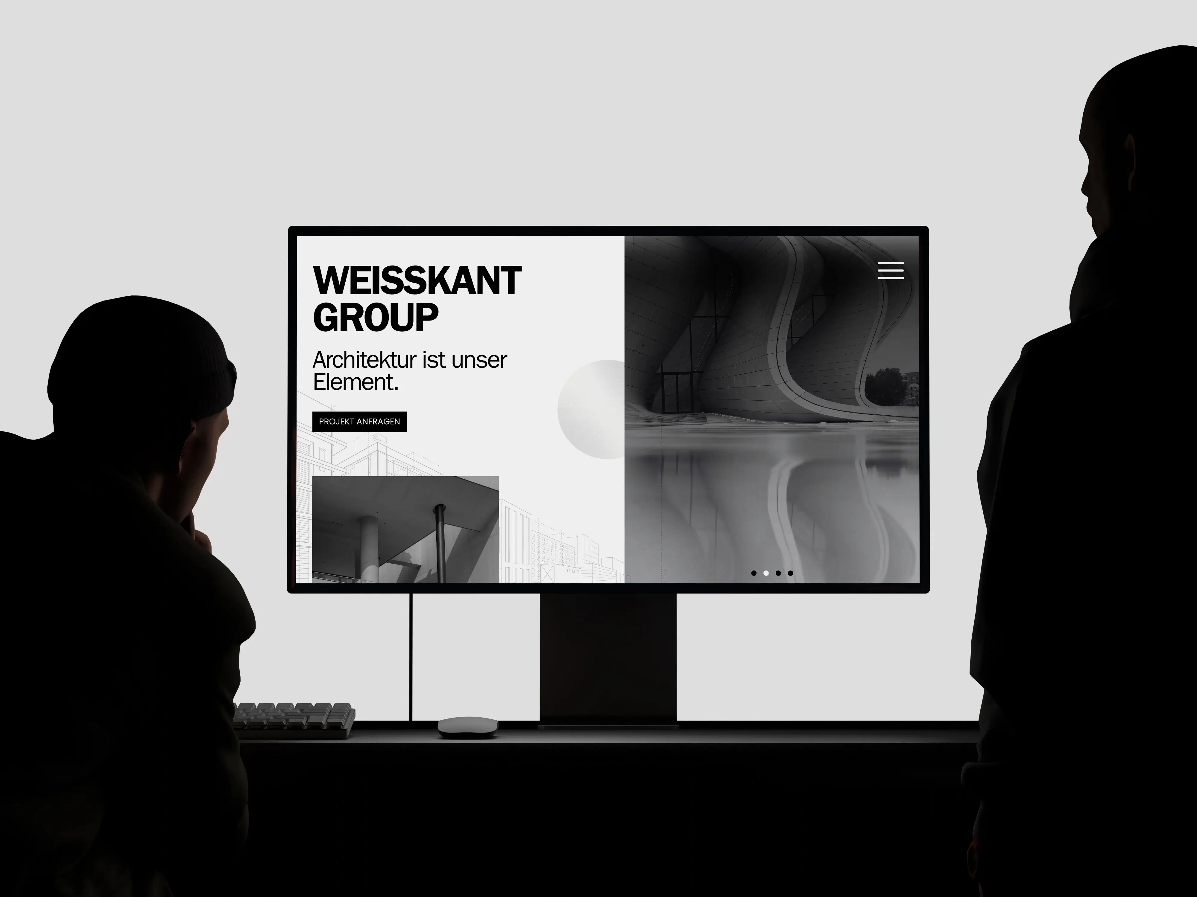 Zwei Personen betrachten einen Desktop-Monitor mit einer Architektur-Website in modernem, minimalistischen Design