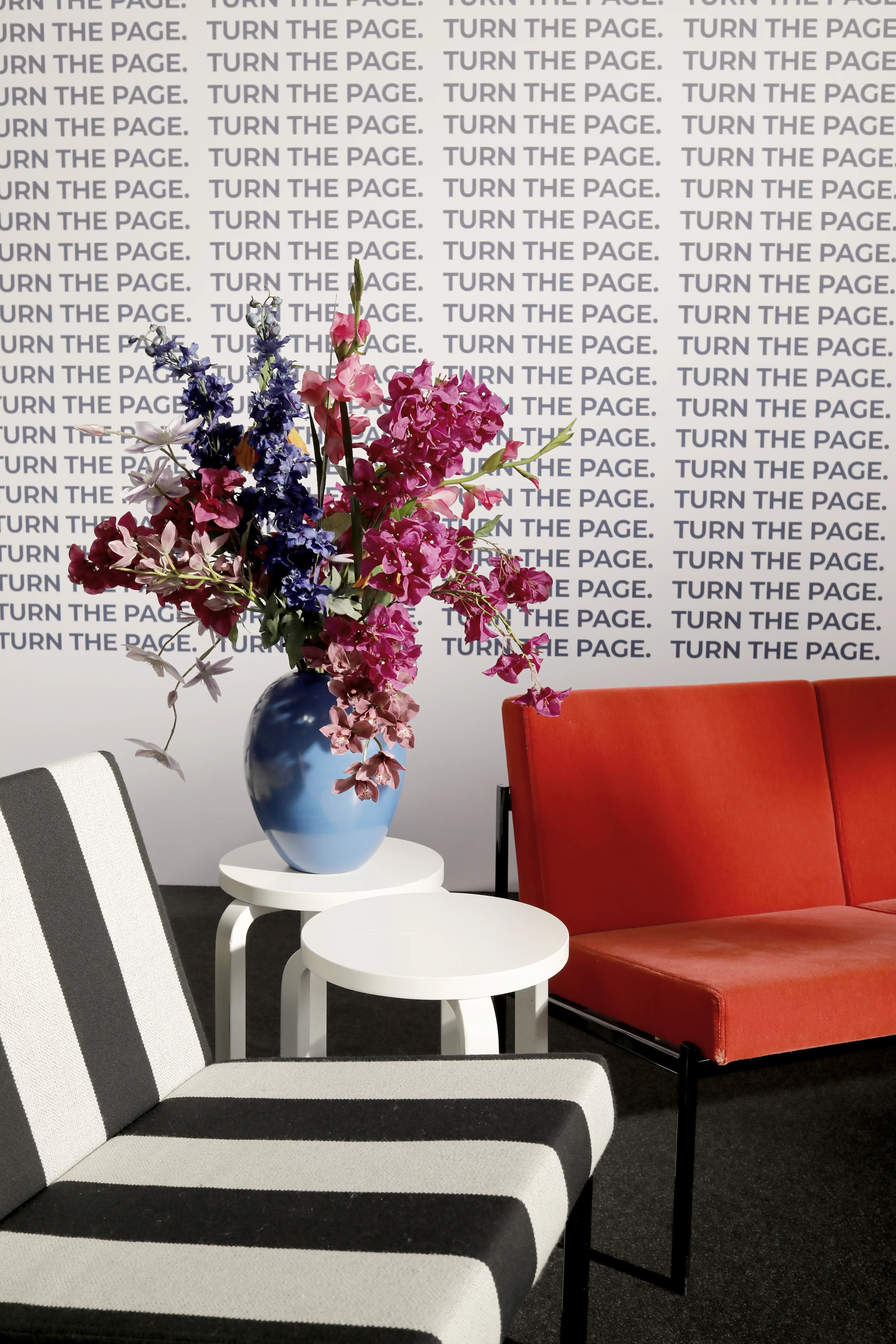 Lounge detail with striped armchairs, a red sofa and a blue vase of flowers in front of the Turn The Page wall at Female Future Force Day.