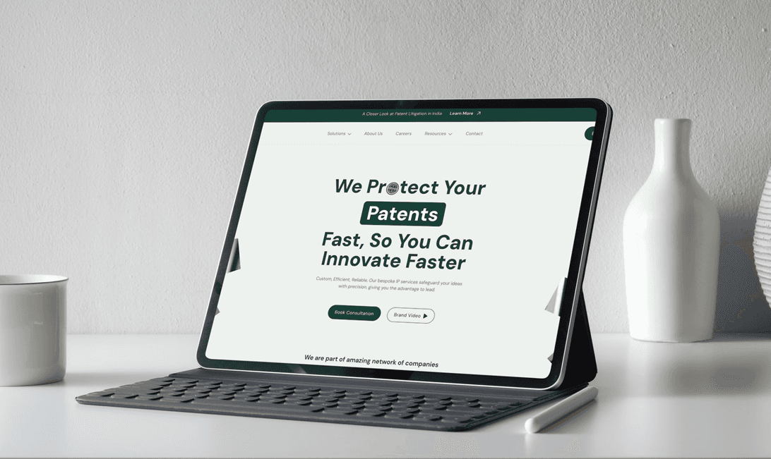 A tablet displaying a website with the title 'We Protect Your Patents Fast, So You Can Innovate Faster'. The tablet is open on a grey keyboard case, next to a white coffee mug and a white decorative vase, on a light grey surface."